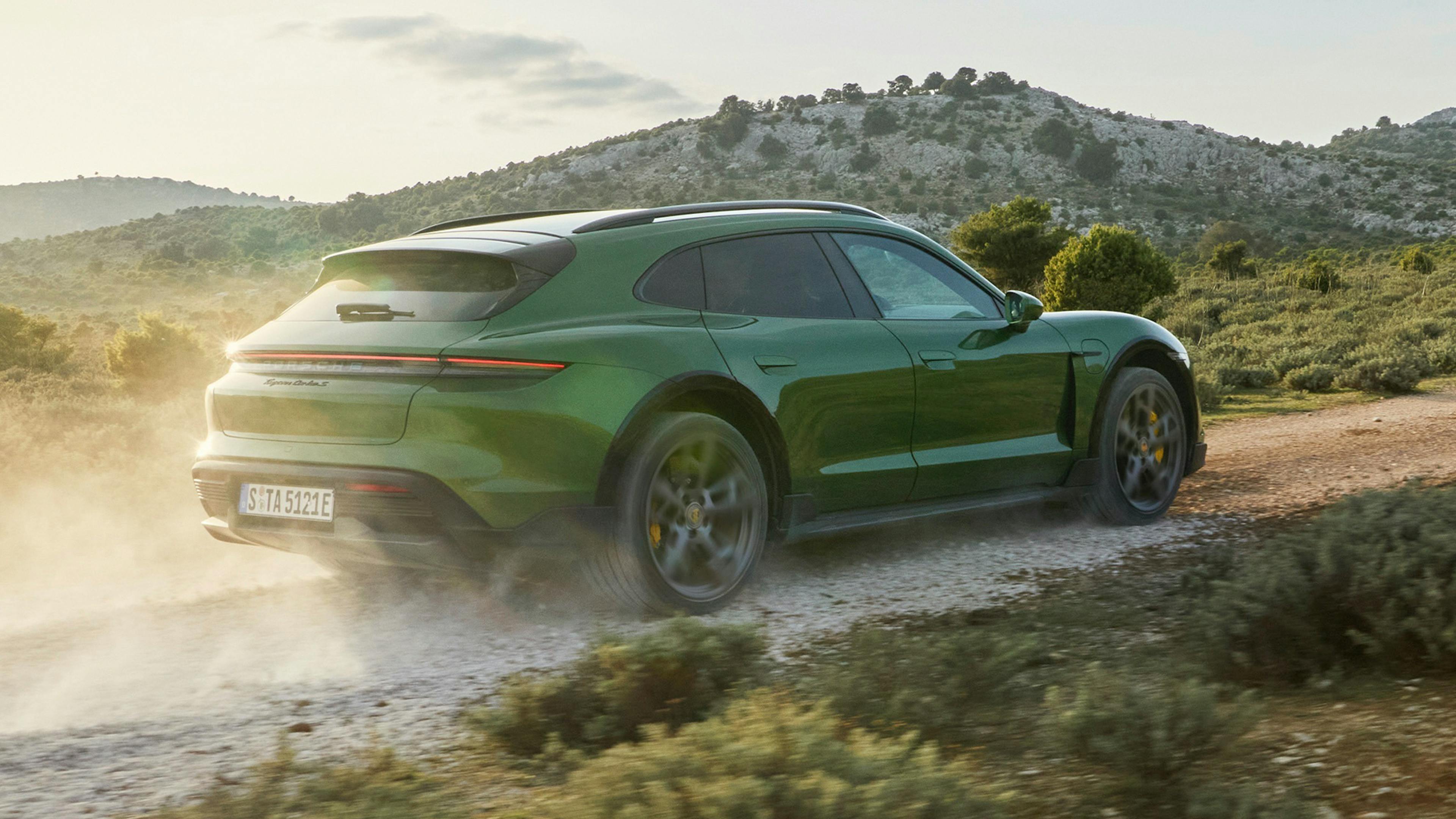 Ein dunkelgrüner Porsche Taycan Cross Tourismo fährt eine Landstraße entlang