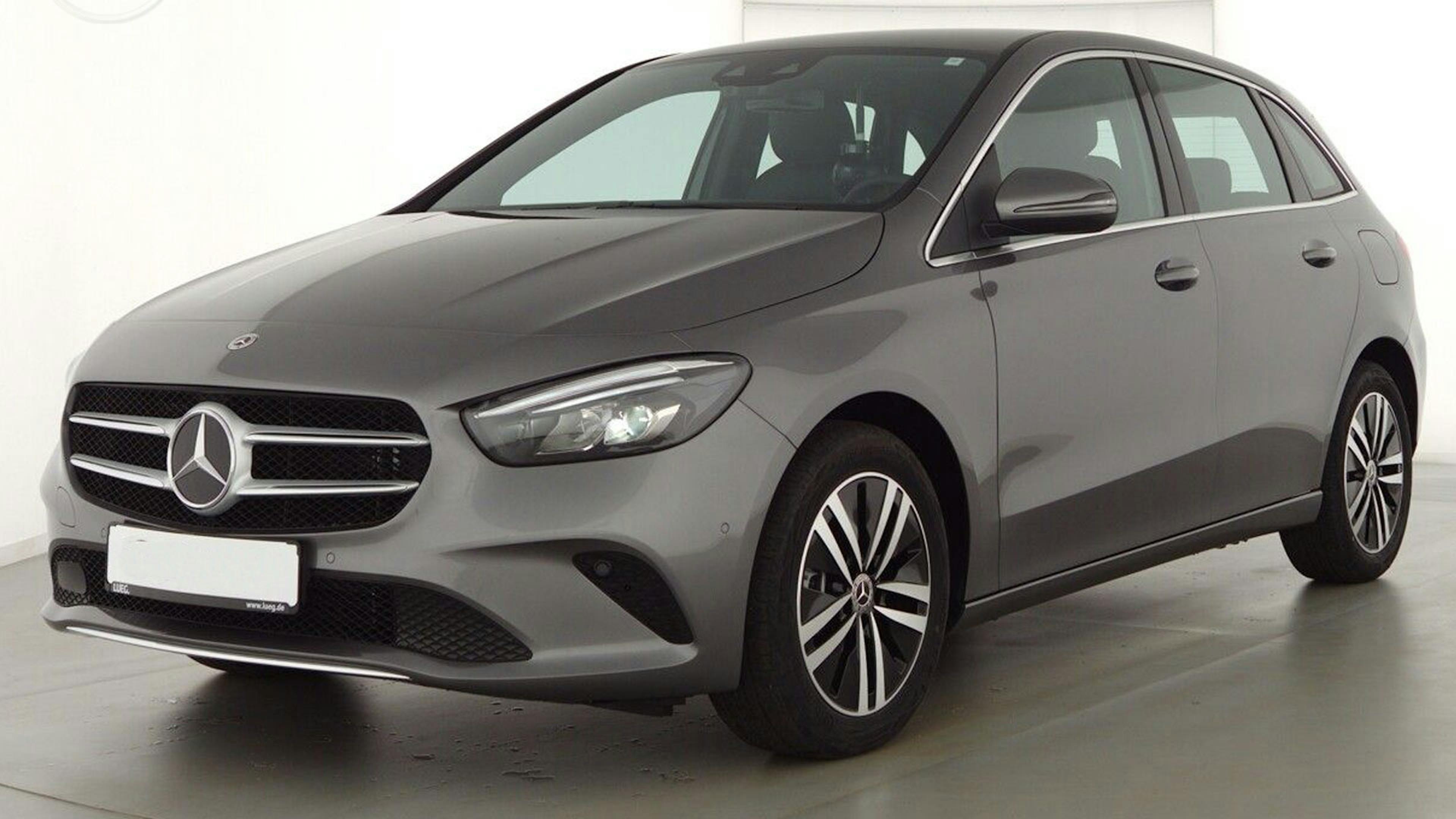 Ein dunkelgrauer Mercedes B250e Plug-in-Hybrid steht vor einer weißen Wand.