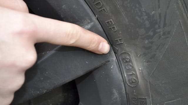 Ein Zeigefinger zeigt auf die DOT-Nummer eines Autoreifens, um das Reifenalter zu bestimmen.