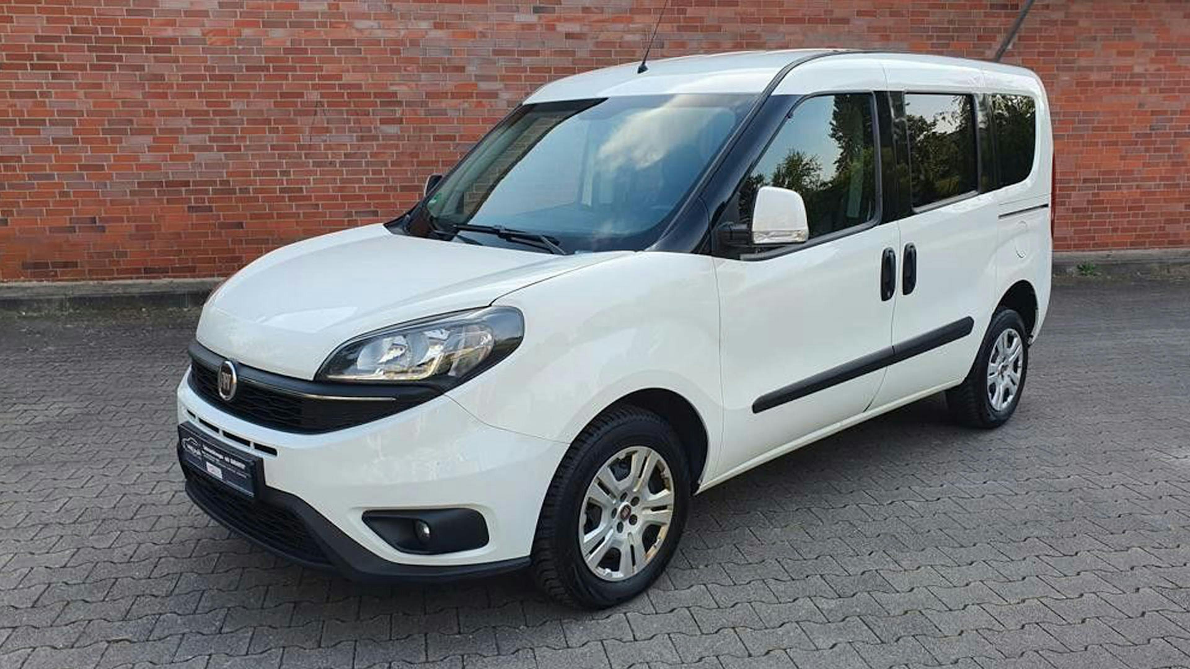 Ein weißer Fiat Doblo Hochdachkombi steht vor einer Backsteinwand.