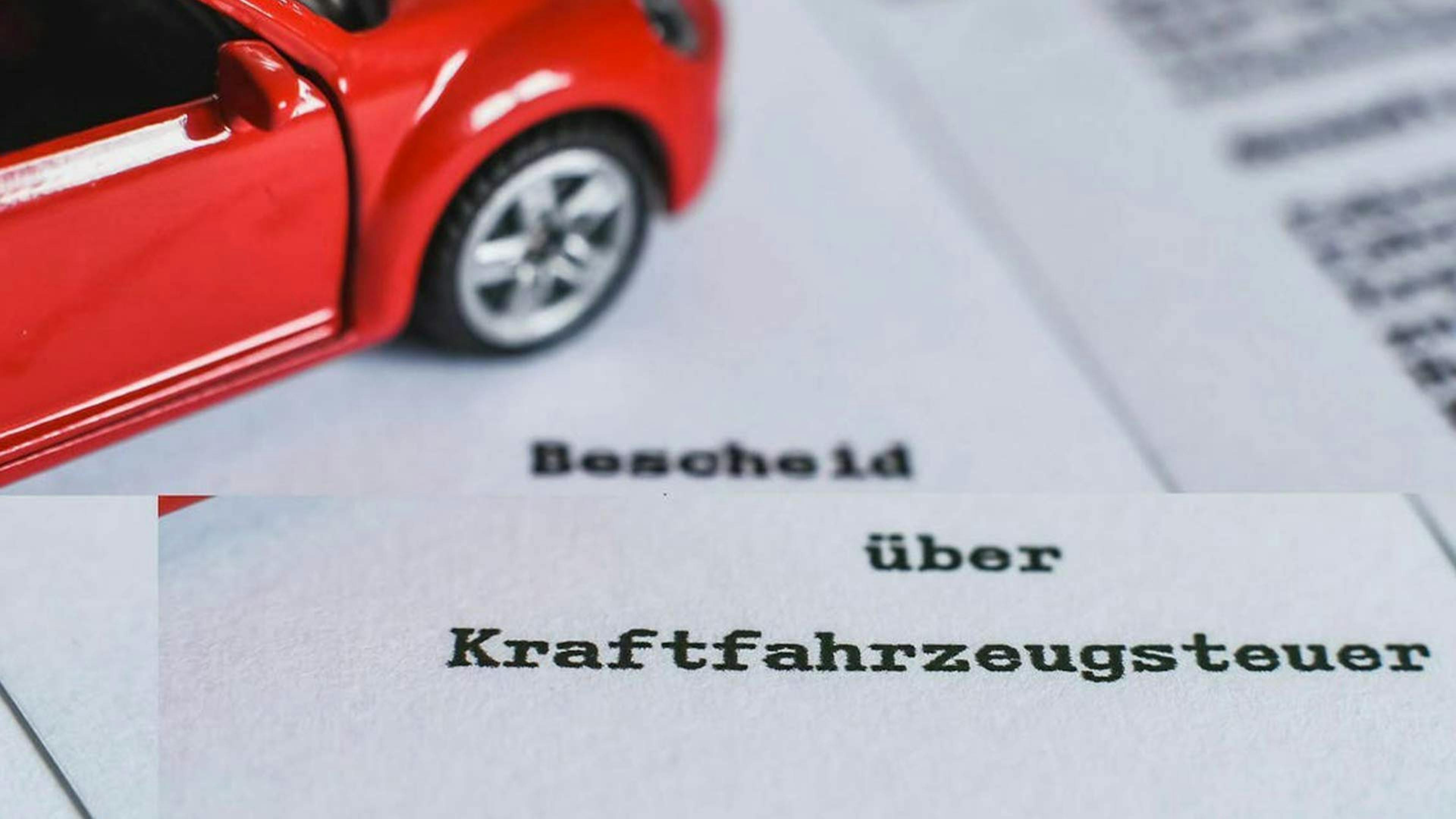 Nahaufnahme eines Kfz-Steuerbescheids und eines roten Spielzeugautos