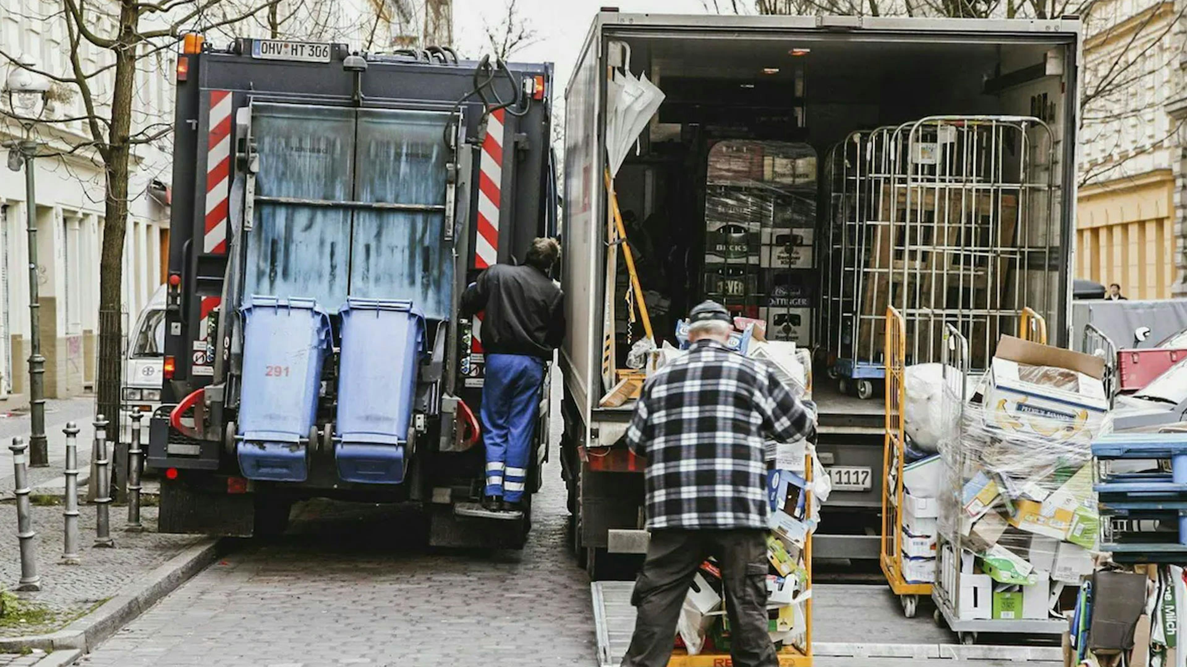 Ein Lkw mit geöffneter Laderampe parkt in zweiter Reihe neben einem Müllabfuhr-Wagen.