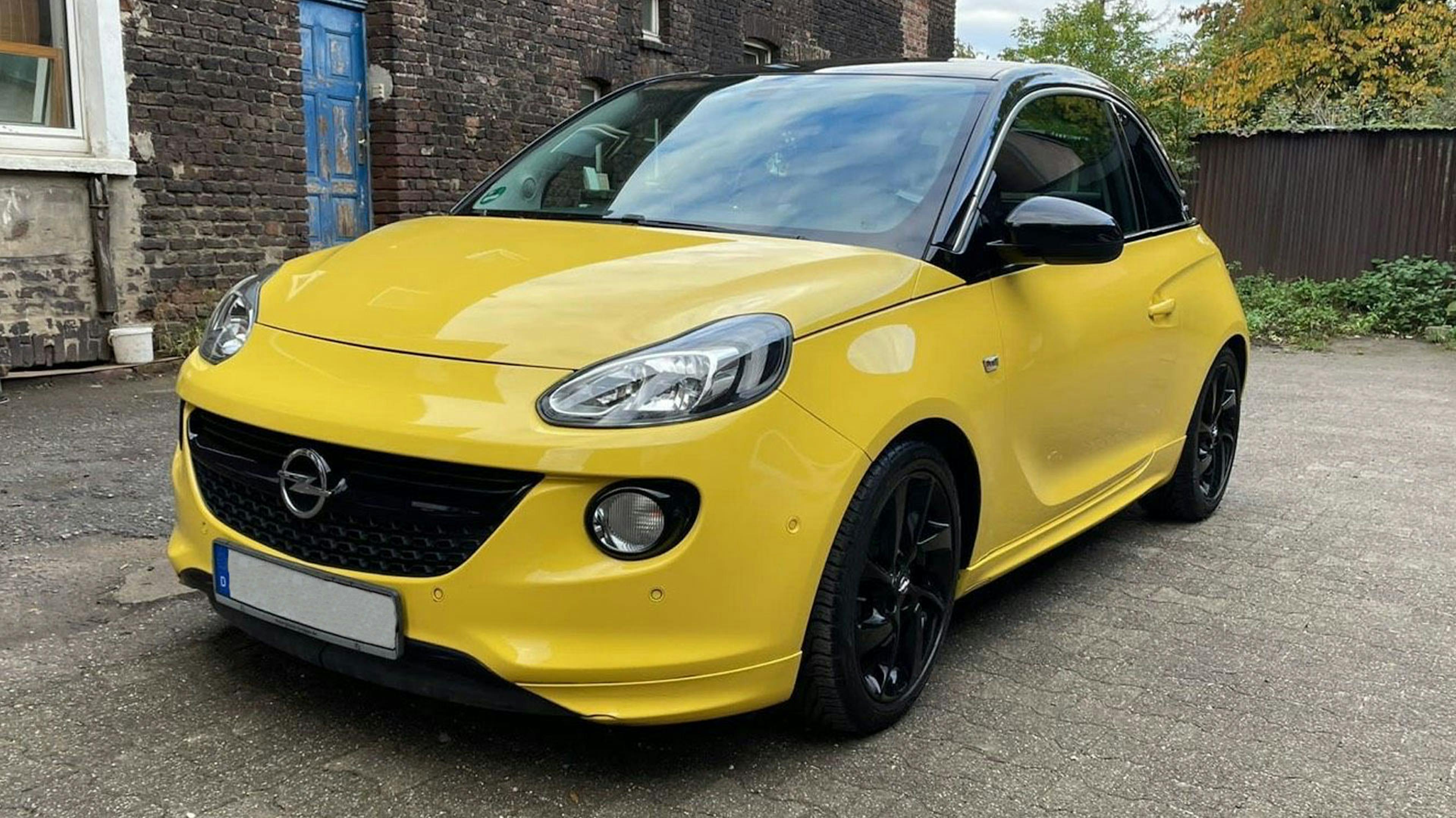 Ein gelber Opel Adam Kleinstwagen steht vor einem Gebäude mit Backsteinfassade.
