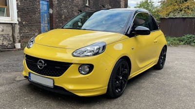 Ein gelber Opel Adam Kleinstwagen steht vor einem Gebäude mit Backsteinfassade.