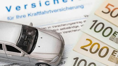 Stillleben mit einem ausgedruckten Kfz-Versicherungsvertrag, Geldscheinen und einem Spielzeugauto.