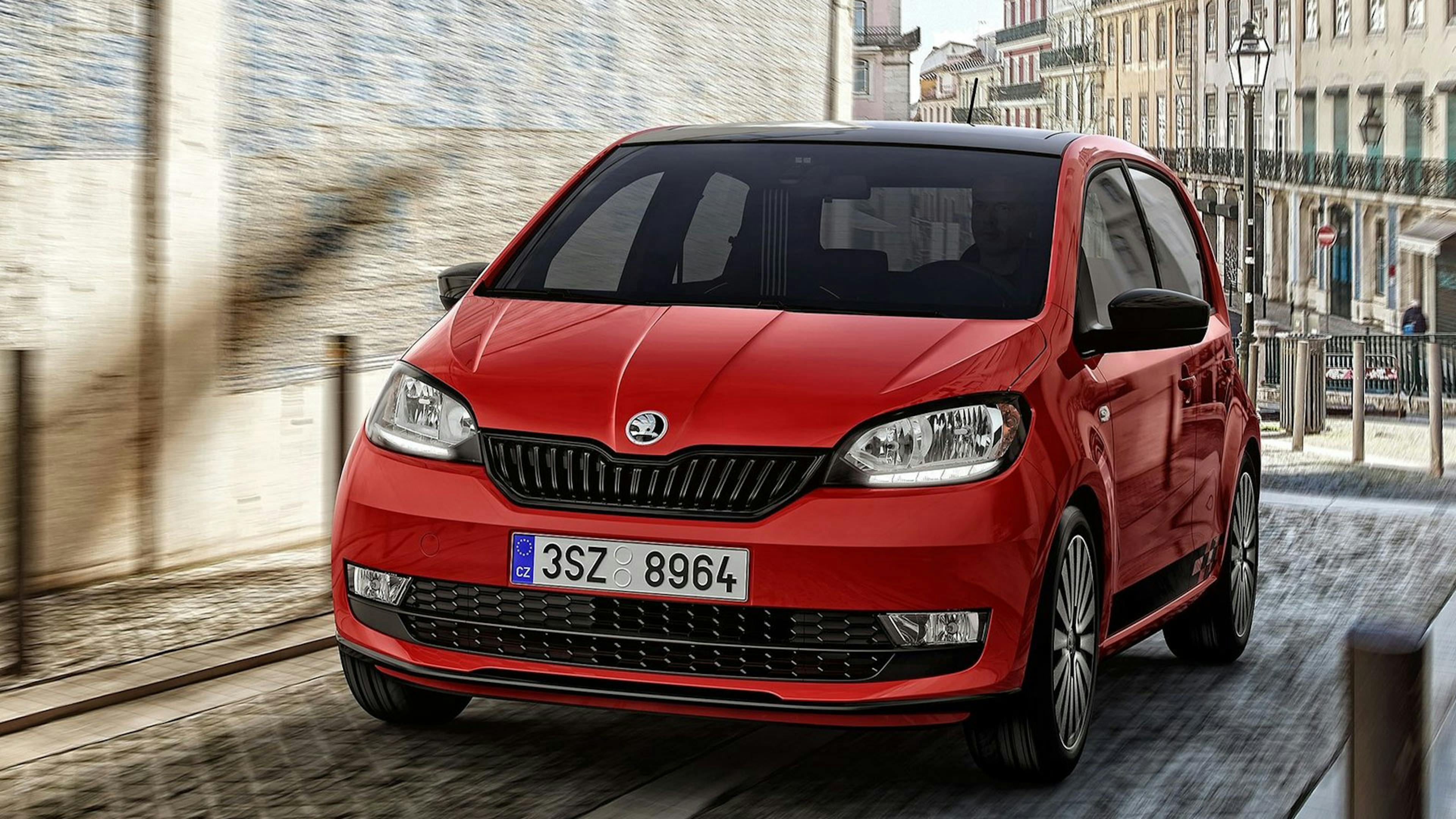 Ein roter Škoda Citigo fährt durch eine enge Straße mit Kopfsteinpflaster.