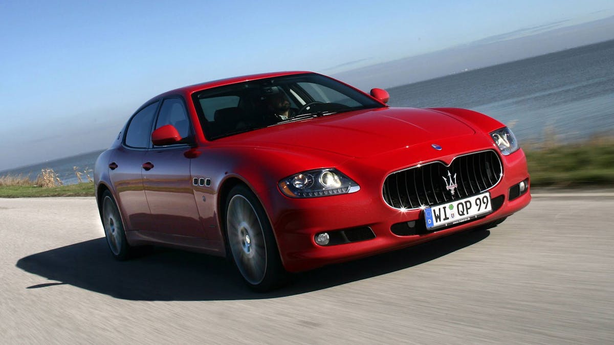 Ein roter Maserati Quattroporte fährt eine Landstraße entlang.