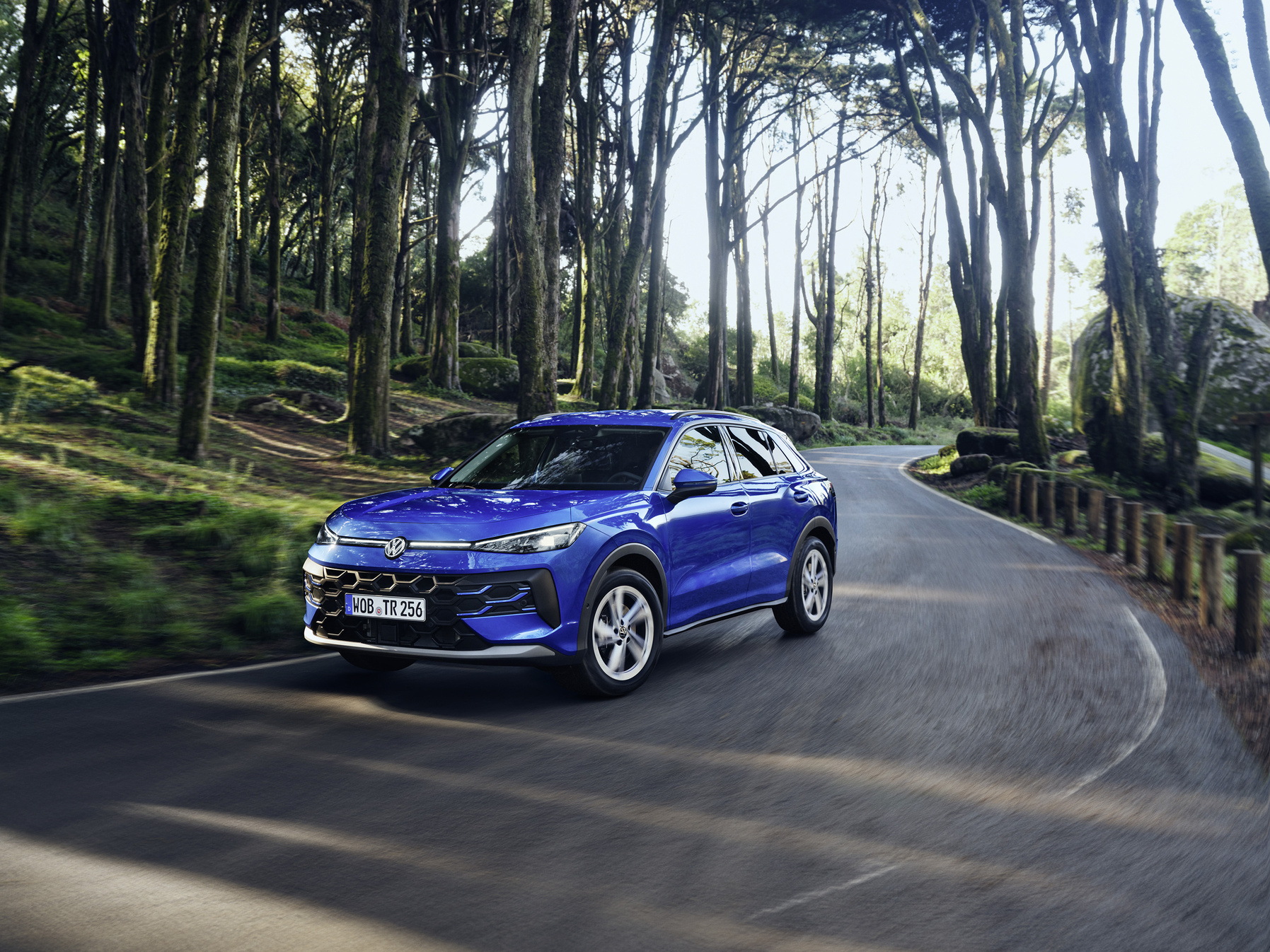 Blauer VW T-Roc, Frontansicht schräg, fahrend auf einer Waldstraße.