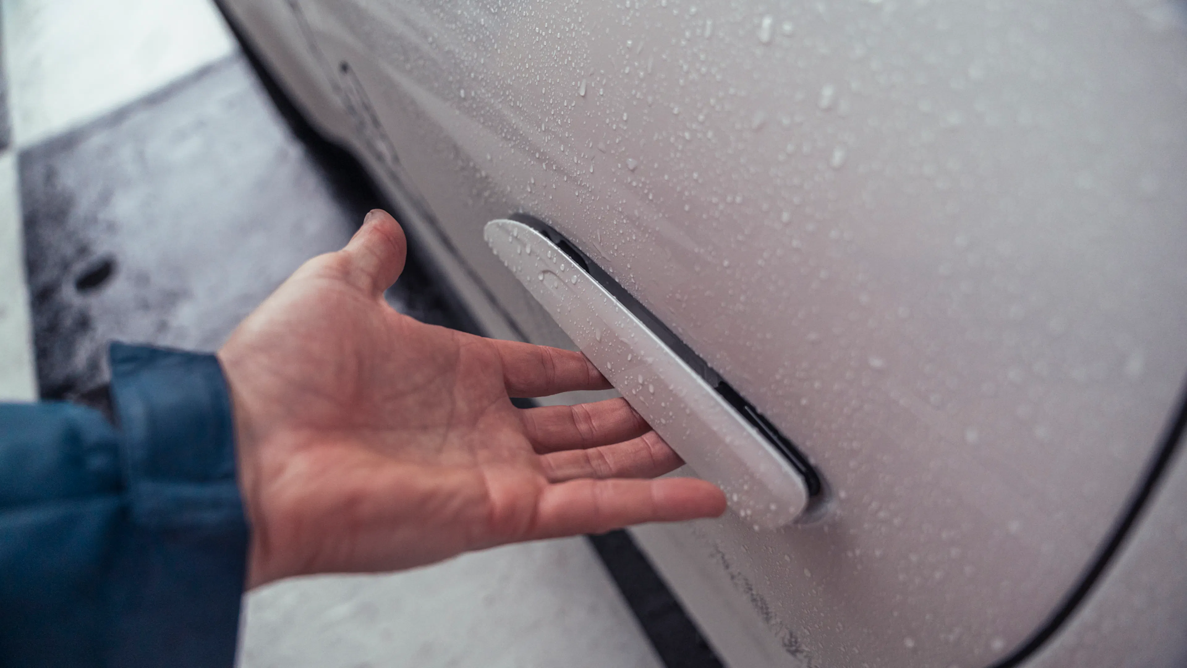 Hand unter einem ausklappbaren, bündig in die weiße Tür integrierten Türgriff des Porsche 911 GT3; auf dem Lack sind Regentropfen zu sehen.