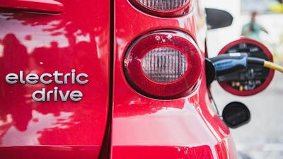Nahaufnahme des Hecks eines roten E-Autos, das aufgeladen wird.