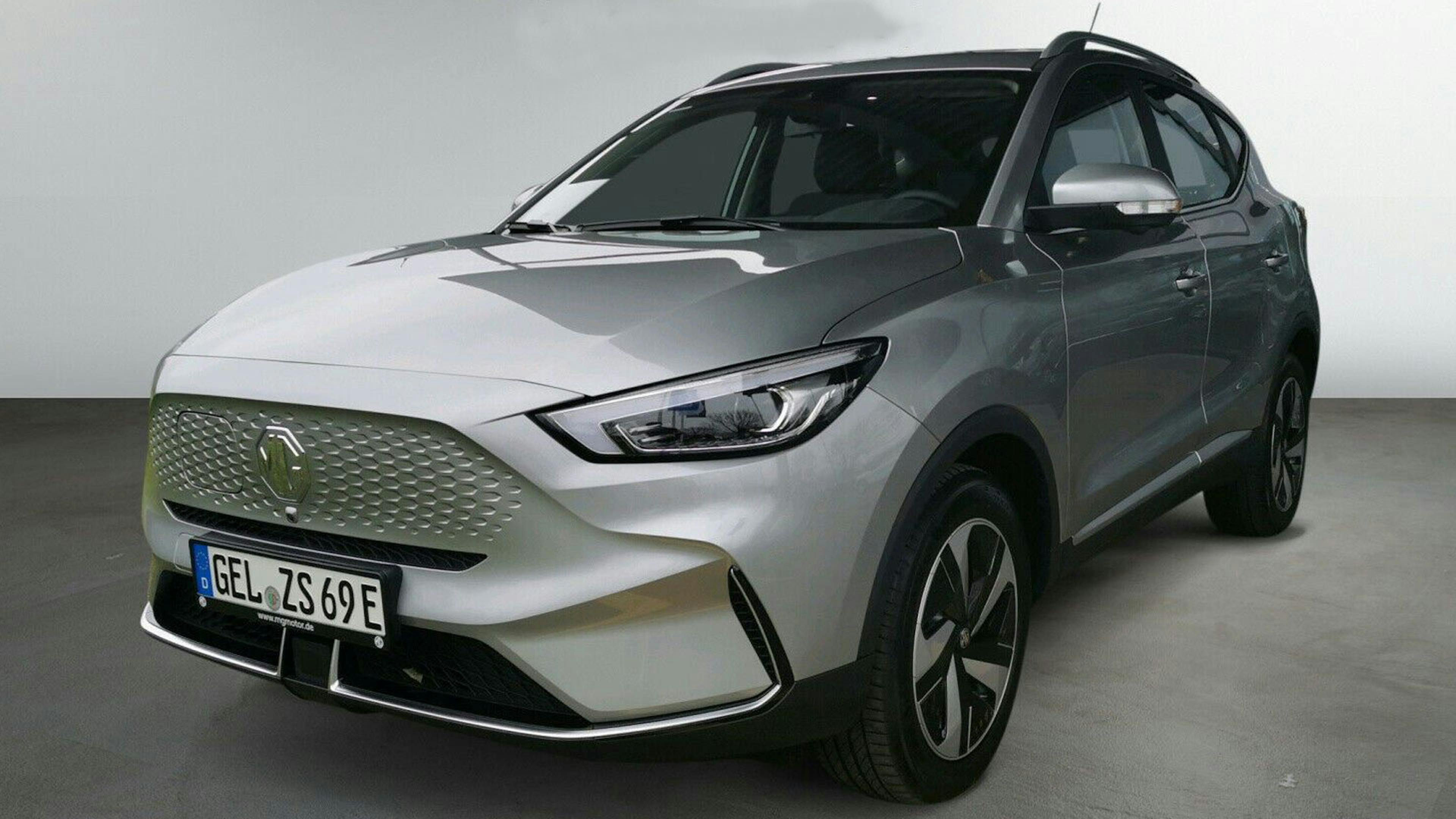 Ein silbernes chinesisches Elektroauto MG ZS EV steht vor einer weißen Wand.