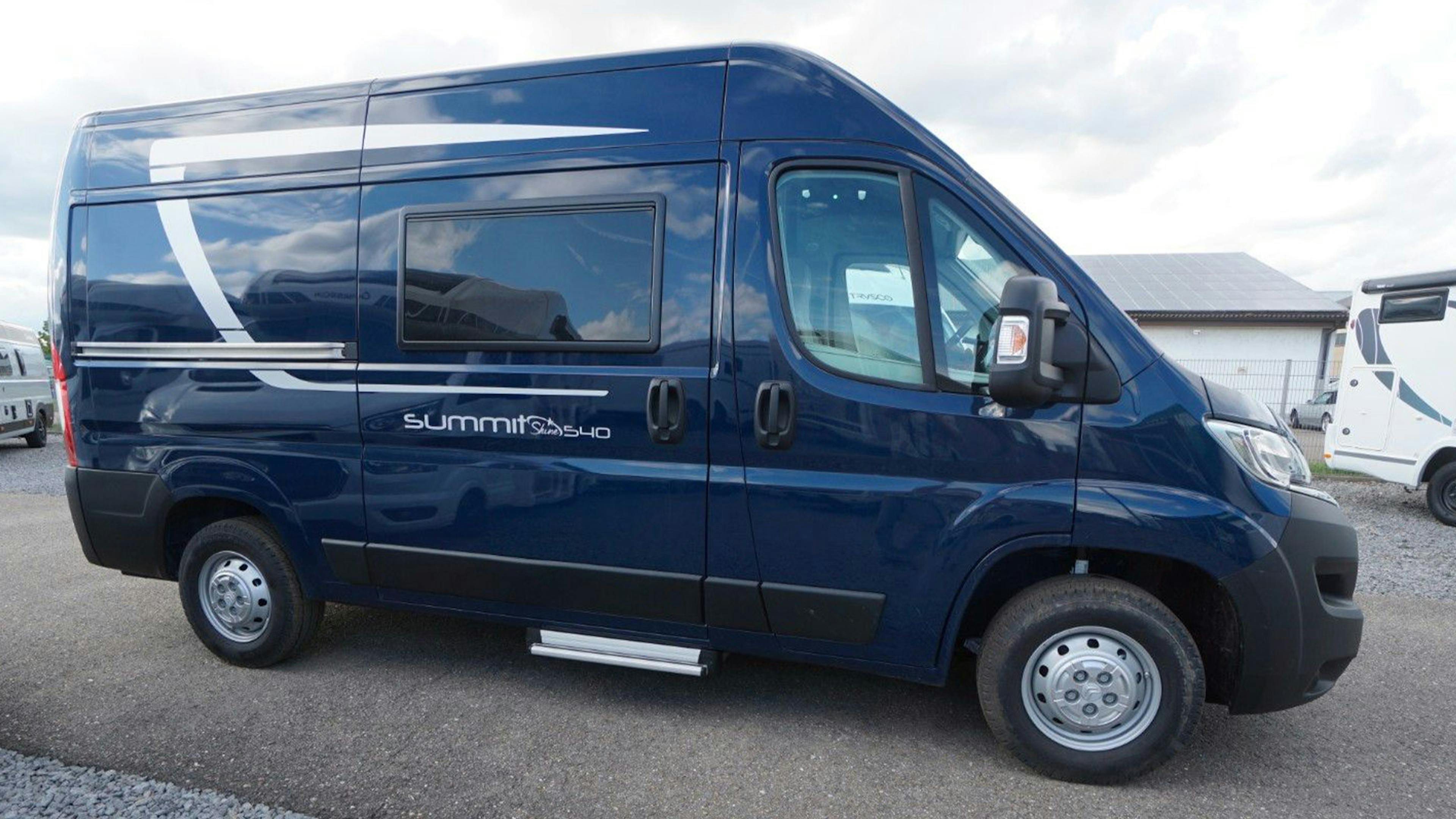 Ein dunkelblauer Pössl Summit 540 Campingbus steht auf einem Parkplatz 