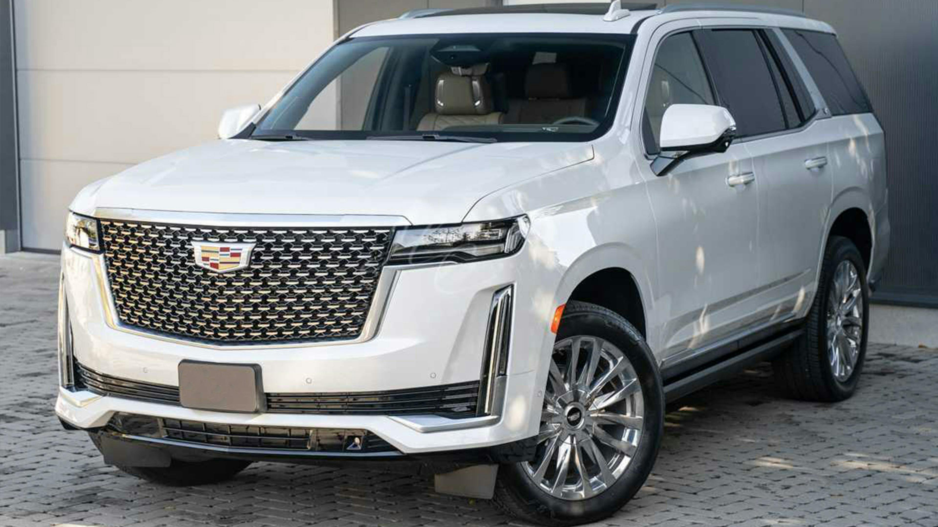 Ein weißer Cadillac Escalade steht vor einem weißen Gebäude mit grauem Rolltor.