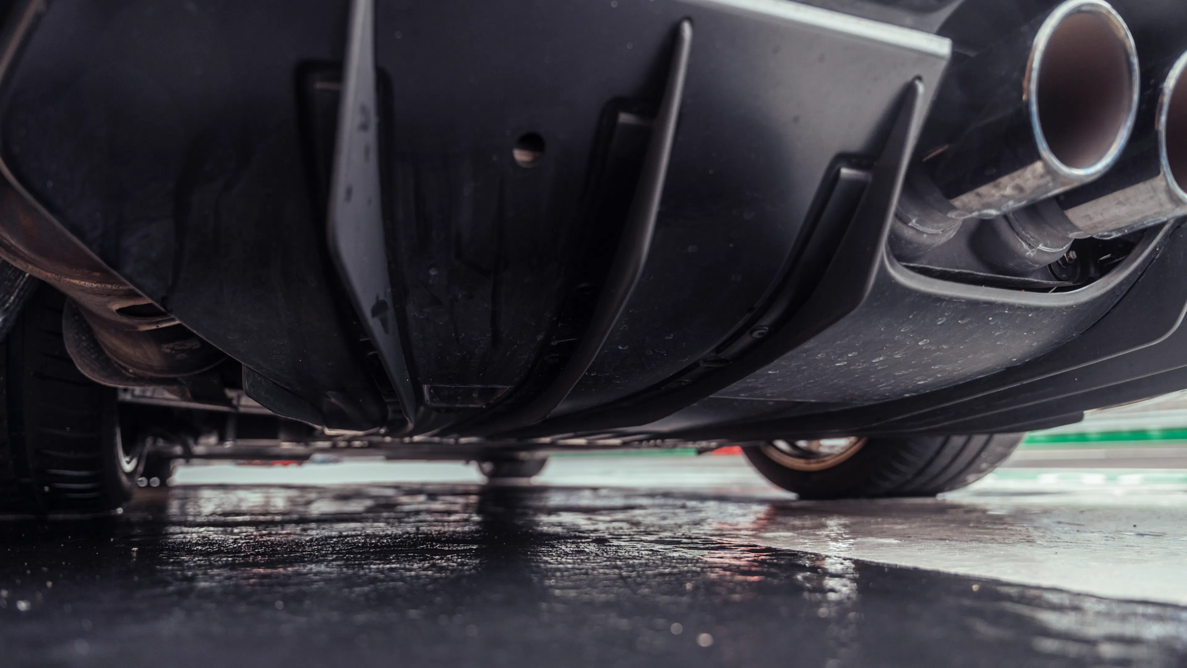 Tiefe Detailaufnahme des nassen Unterbodens eines Porsche 911 GT3 (992.2) mit schwarzem Diffusor, sichtbaren Fahrwerks- und Abgaskomponenten sowie zwei zentralen Endrohren.
