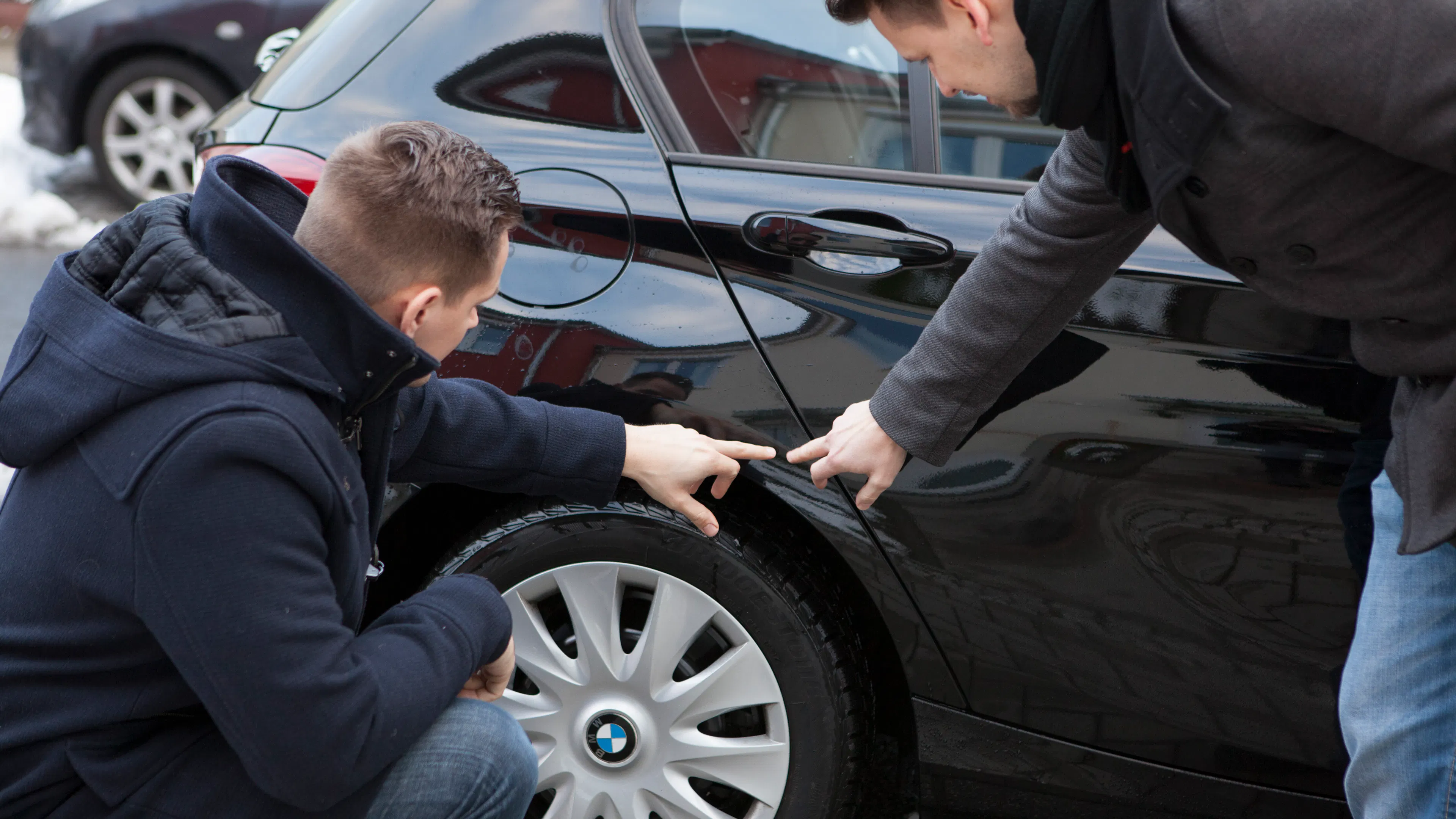 Zwei Männer zeigen auf eine Schadstelle am hinteren Kotflügel eines schwarzen BMW