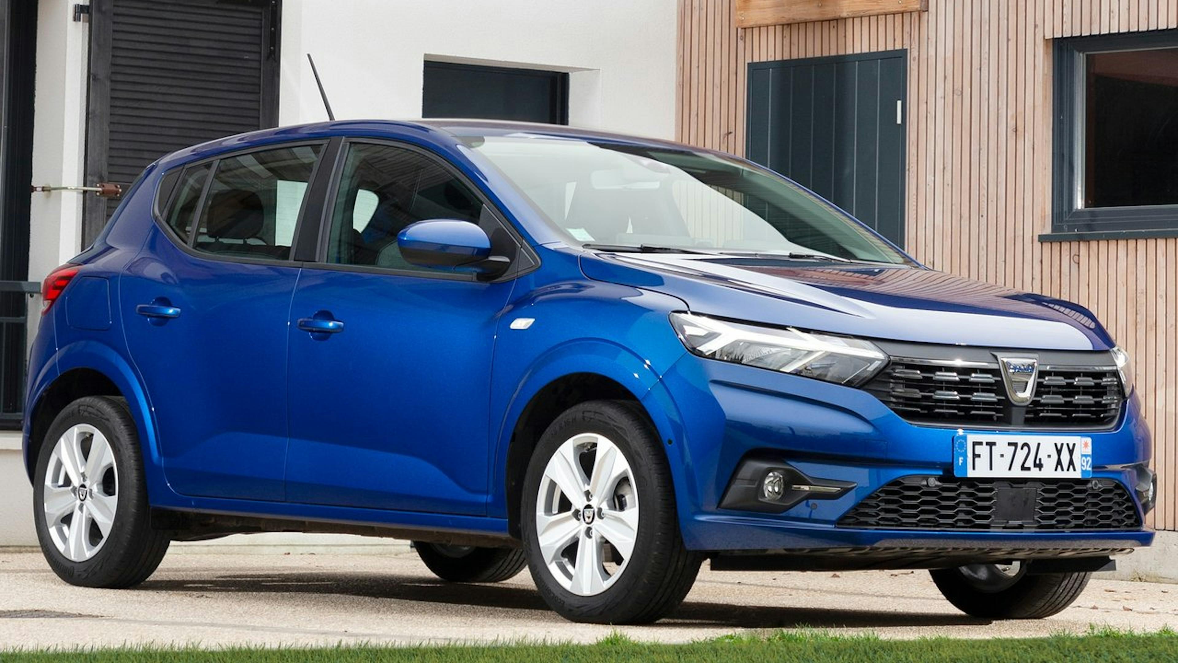 A blue Dacia Sandero is parked in front of a house.