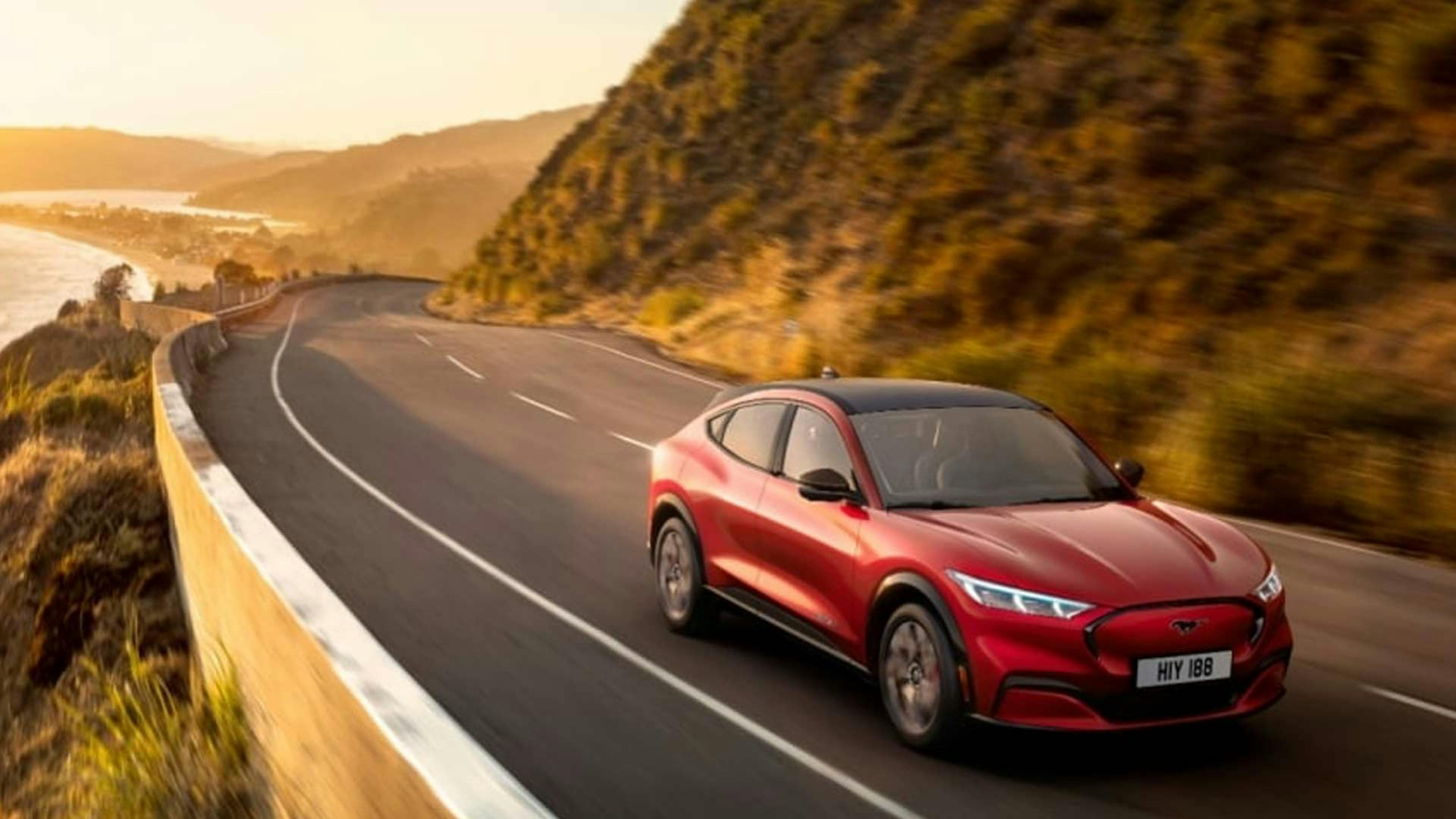 Ein roter Ford Mustang Mach-E fährt eine kurvige Küstenstraße entlang.