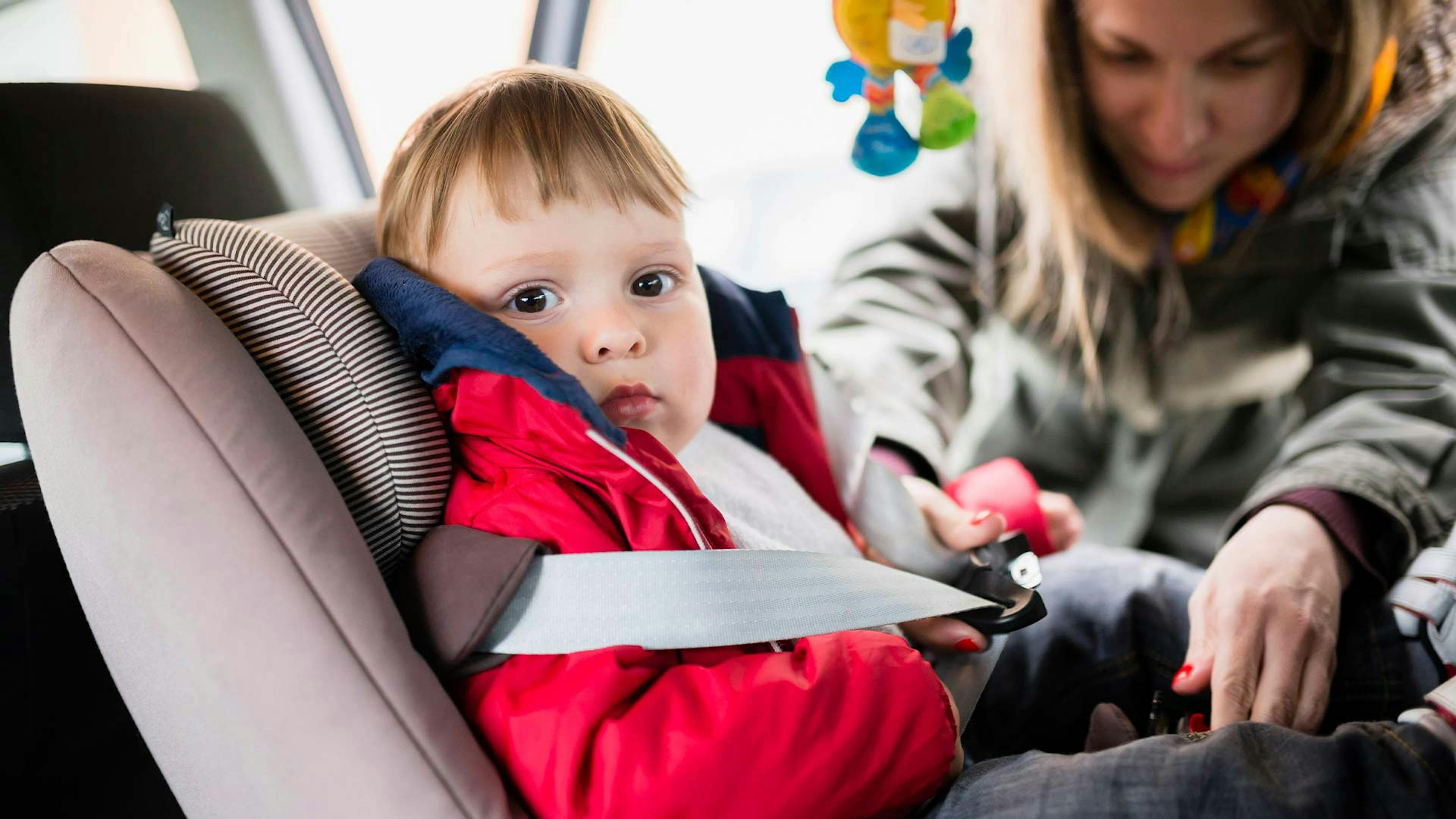 Eine Frau schnallt ein Kleinkind in einem Kindersitz mit Isofix-System in einem Auto an.