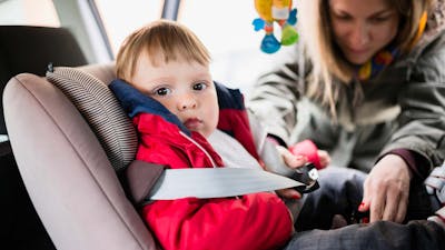 Eine Frau schnallt ein Kleinkind in einem Kindersitz mit Isofix-System in einem Auto an.
