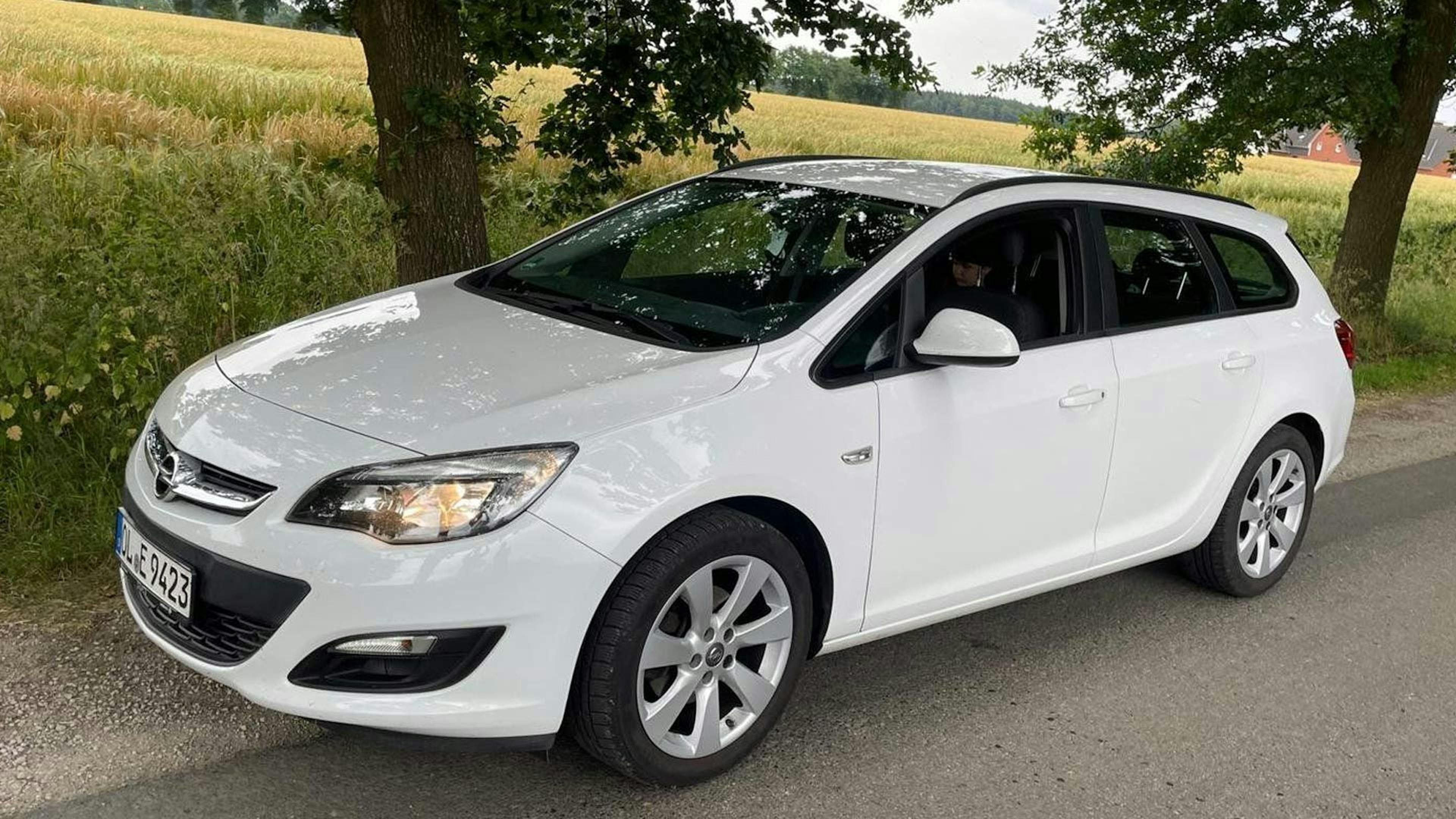 Ein weißer Opel Astra J Sports Tourer-Kombi steht am Rand einer Landstraße.