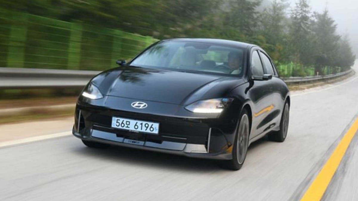 Ein schwarzes Hyundai Ioniq 6 Elektroauto fährt eine Landstraße entlang.