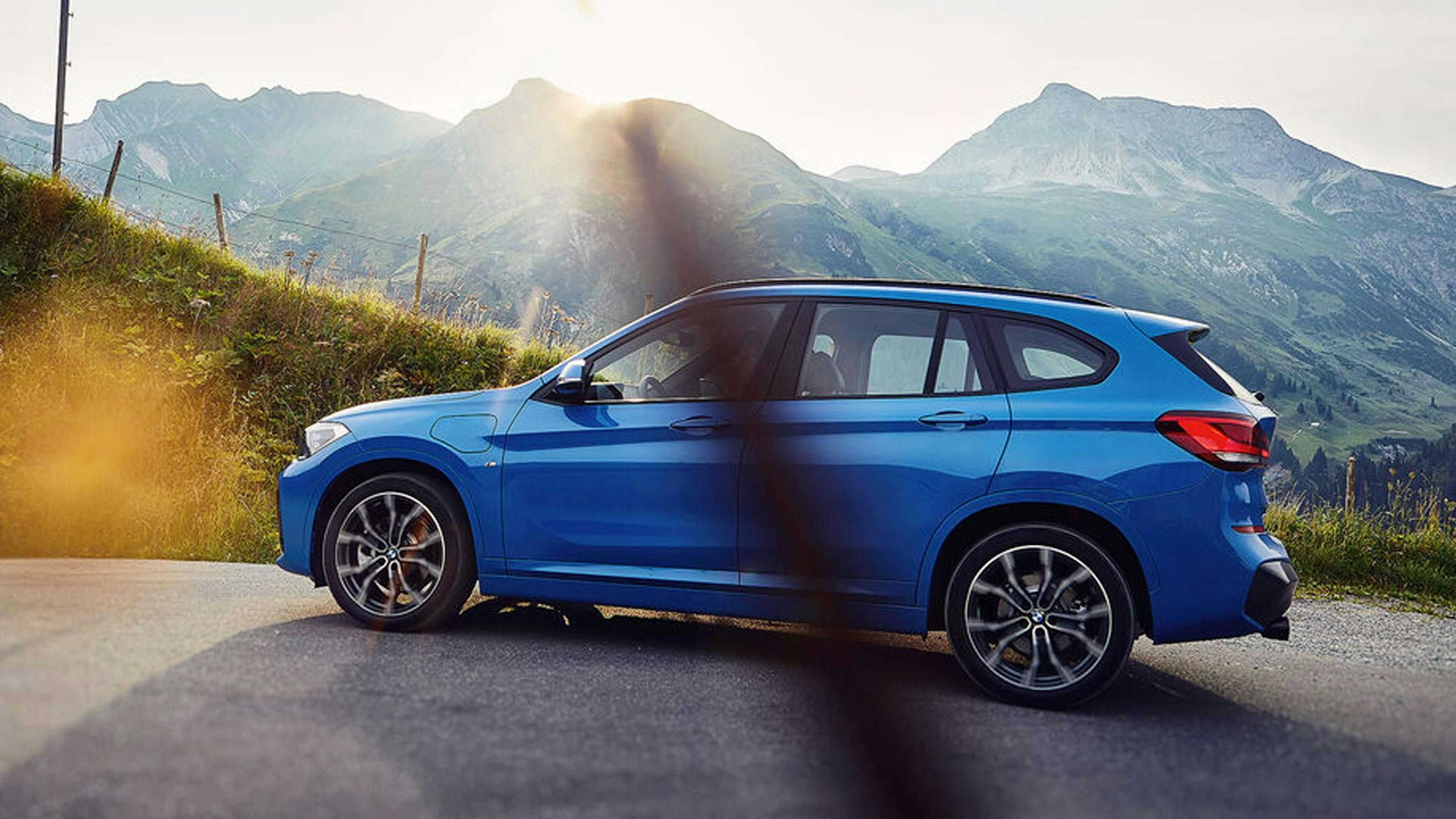 Ein blauer BMW X1 xDrive25e steht vor einem Bergpanorama.