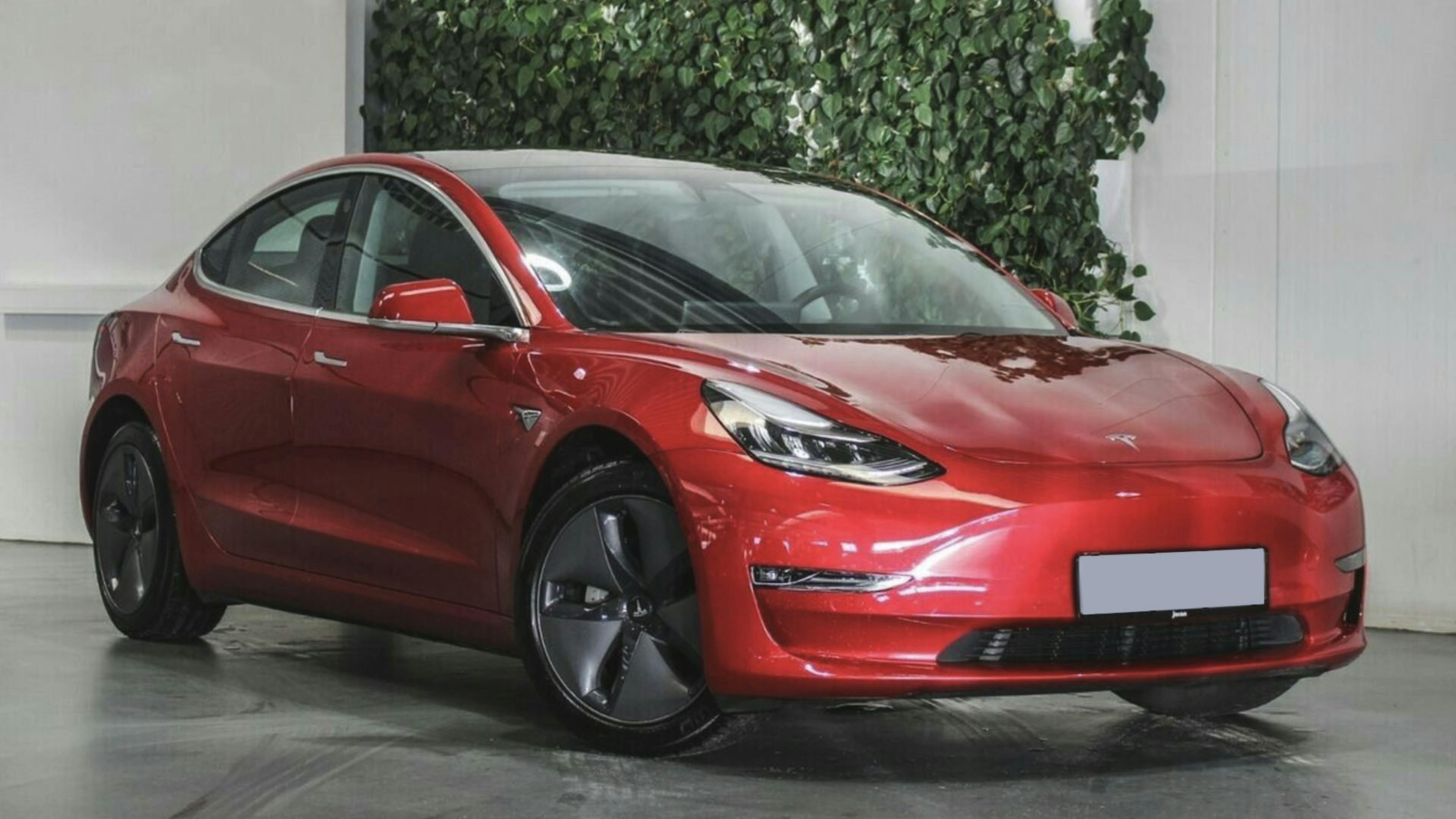 Ein rotes Tesla Model 3 Elektroauto mit Allradantrieb steht in einem Autohaus.