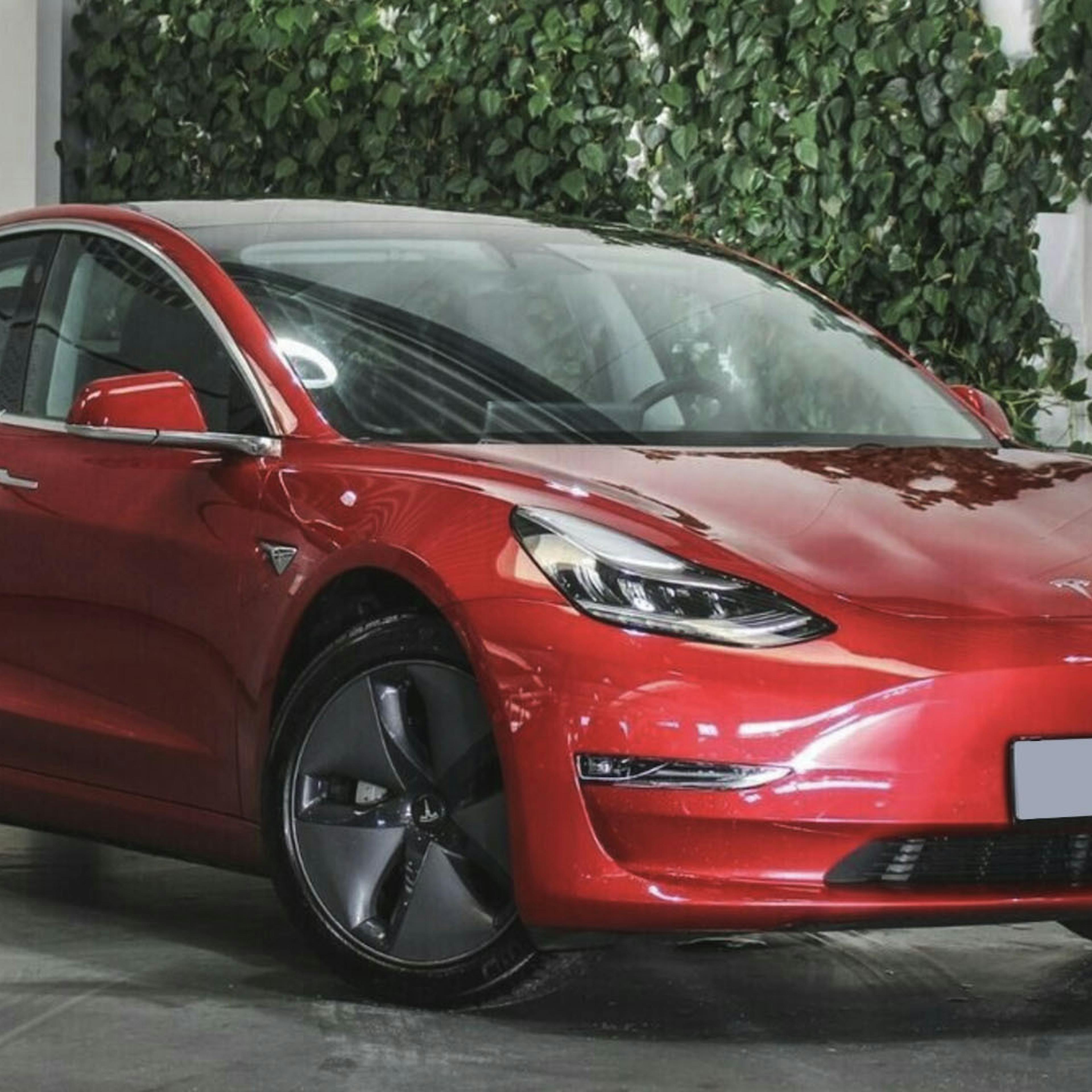 Ein rotes Tesla Model 3 Elektroauto mit Allradantrieb steht in einem Autohaus.