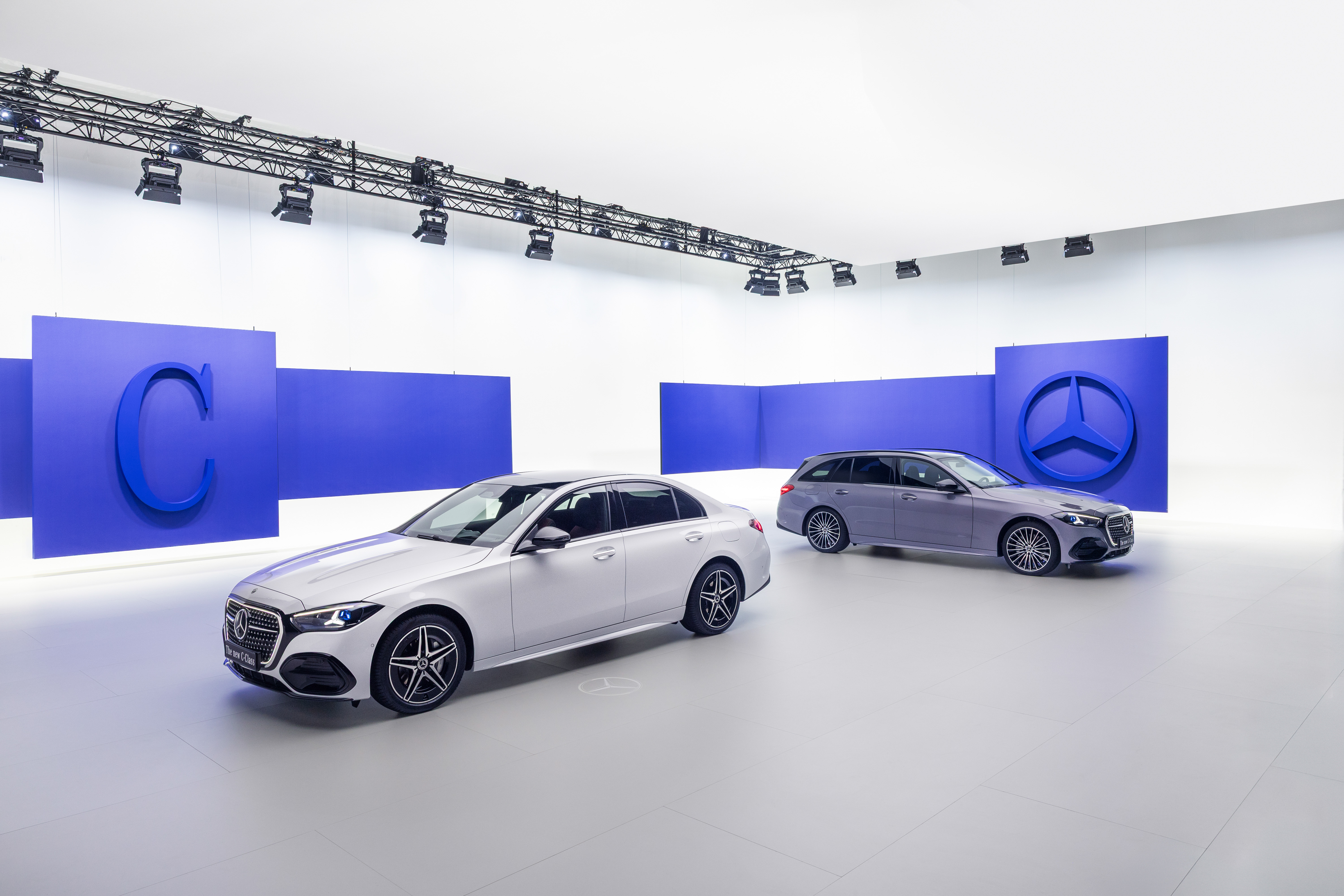 Mercedes-Benz C-Klasse Limousine und T-Modell 2026 nebeneinander im Studio vor blauem Hintergrund mit C-Logo und Mercedes-Stern.
