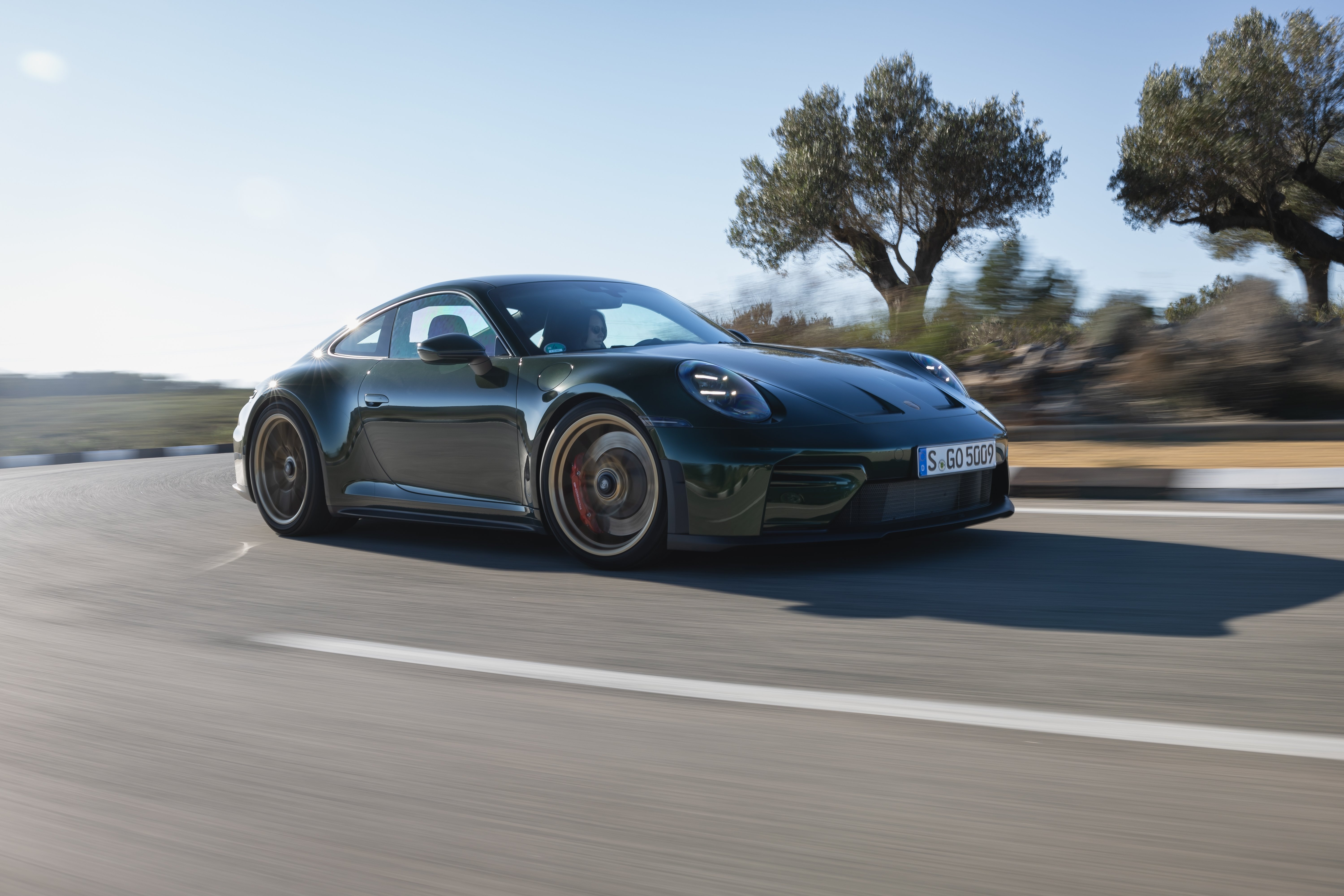 Porsche 911 GT3 fährt dynamisch auf einer Landstraße, Seitenansicht von vorn.