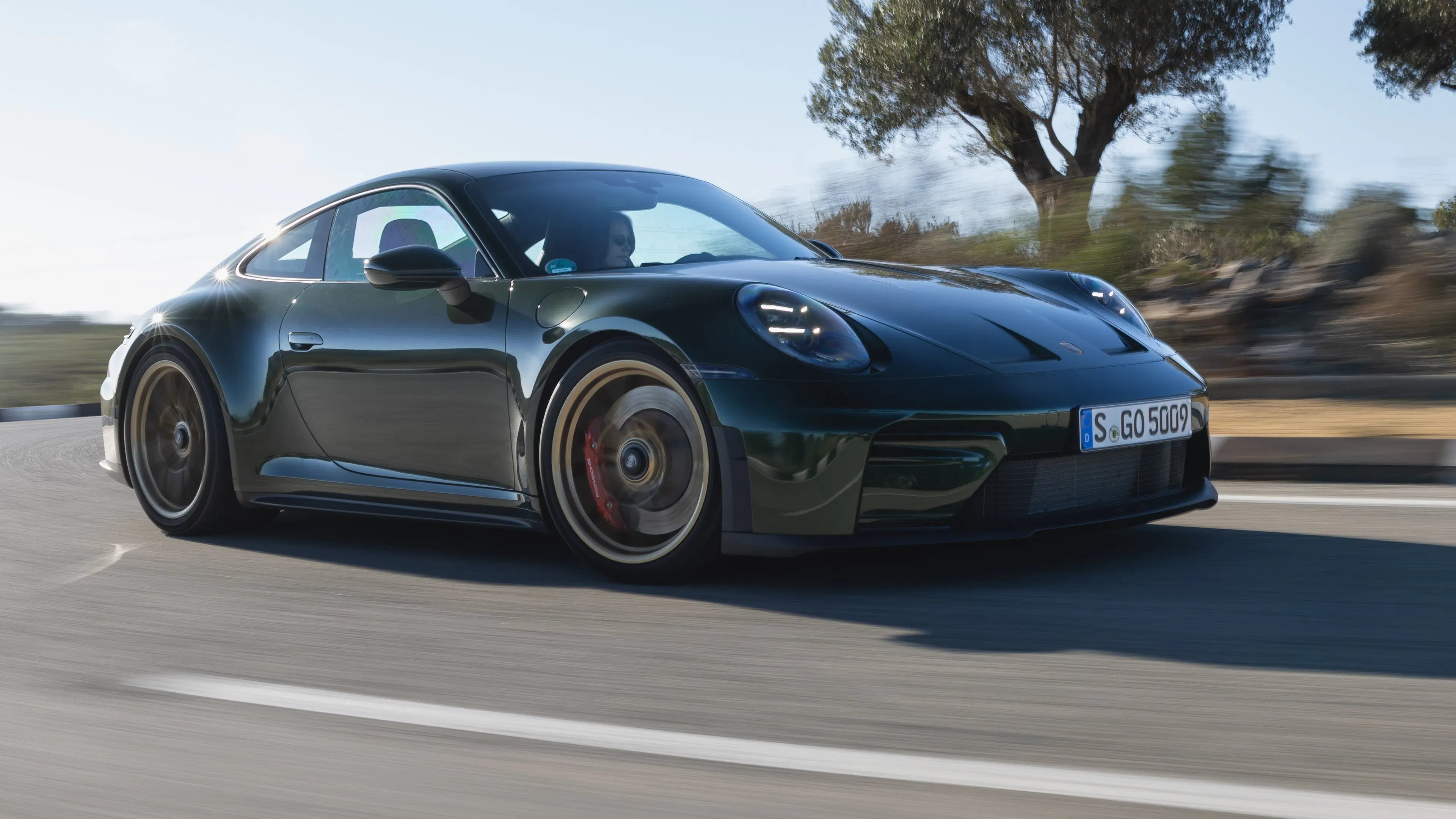 Porsche 911 GT3 fährt dynamisch auf einer Landstraße, Seitenansicht von vorn.