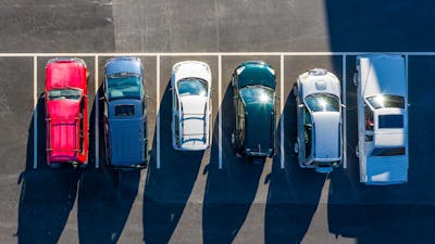 Luftaufnahme von sechs Pkw verschiedener Fahrzeugklassen, die auf einem Parkplatz stehen