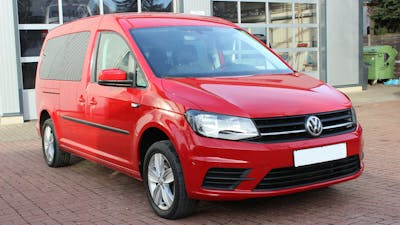 Ein roter VW Caddy Hochdachkombi steht vor einem hellen Gebäude.