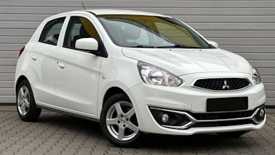 Ein weißer Mitsubishi Space Star steht vor einem grauen Rolltor.