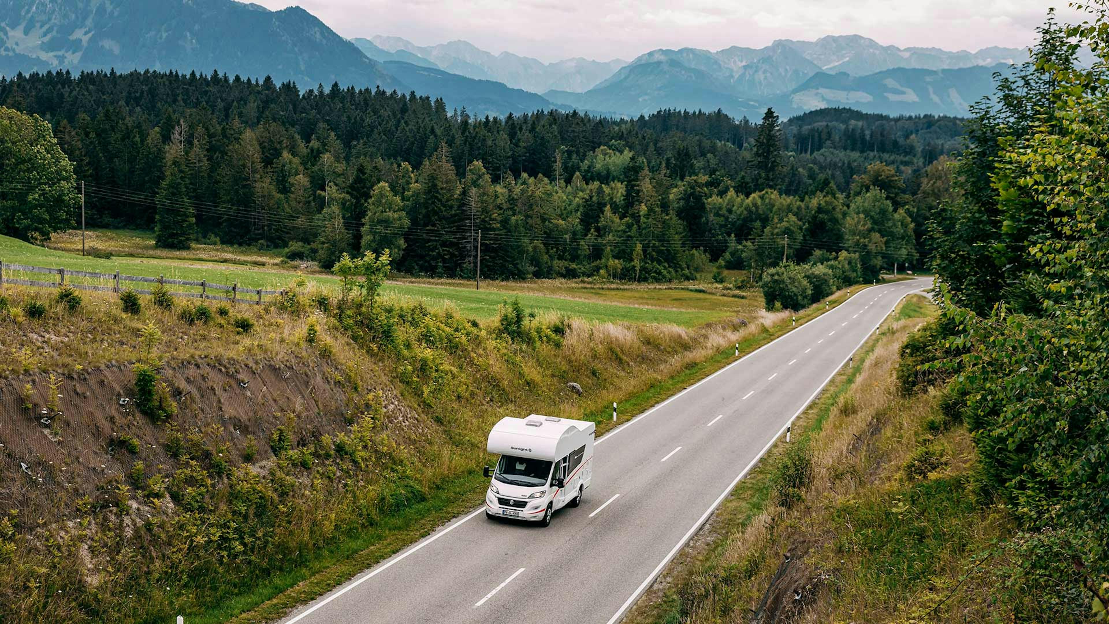 Ein Sunlight A 60-Wohnmobil mit Alkoven fährt eine Landstraße entlang. 