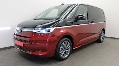 Ein rot-grauer VW T7 Plug-in-Hybrid steht vor einer weißen Wand
