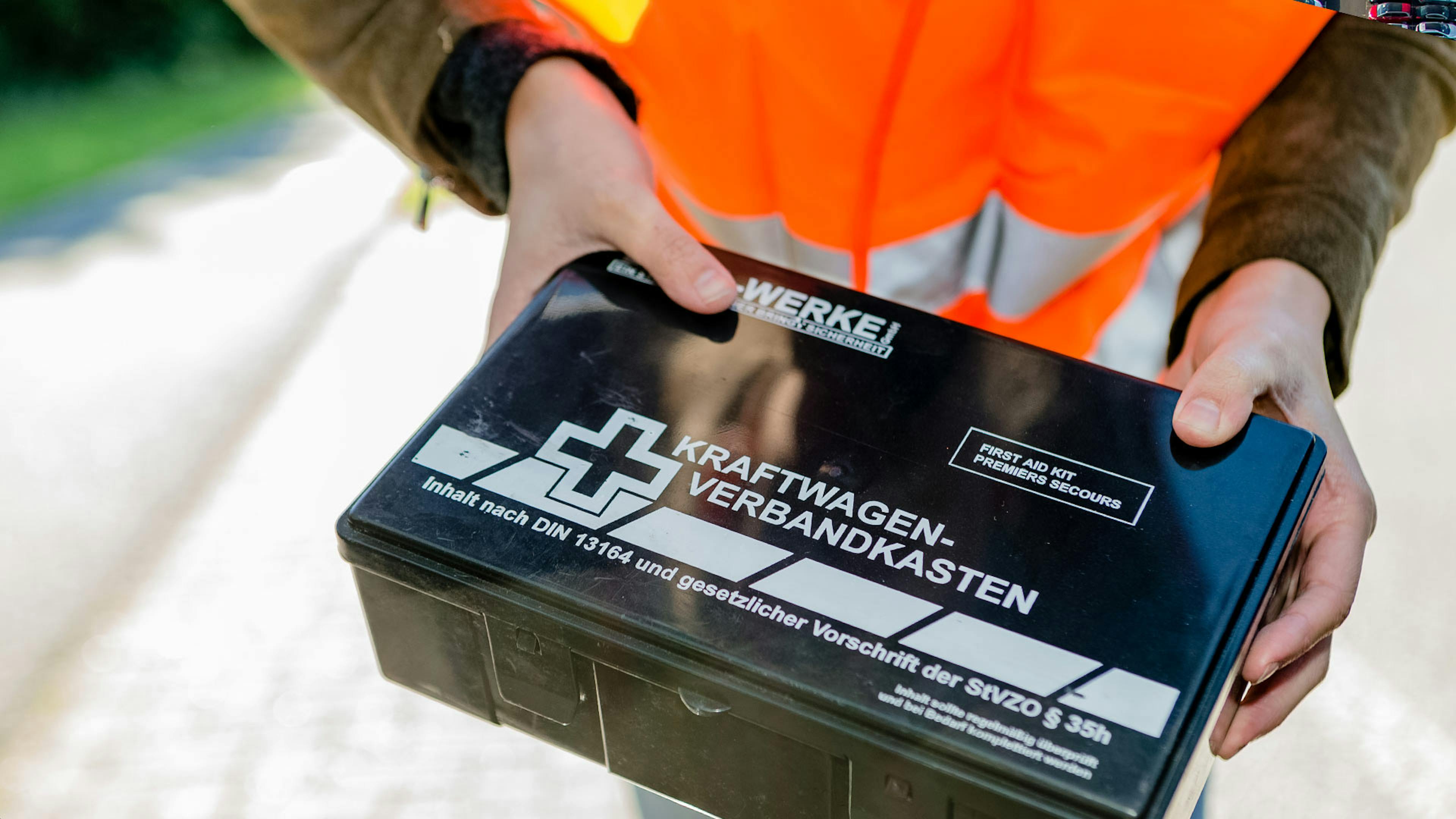 Eine Person mit Warnweste hält einen Kraftwagen-Verbandkasten in den Händen.