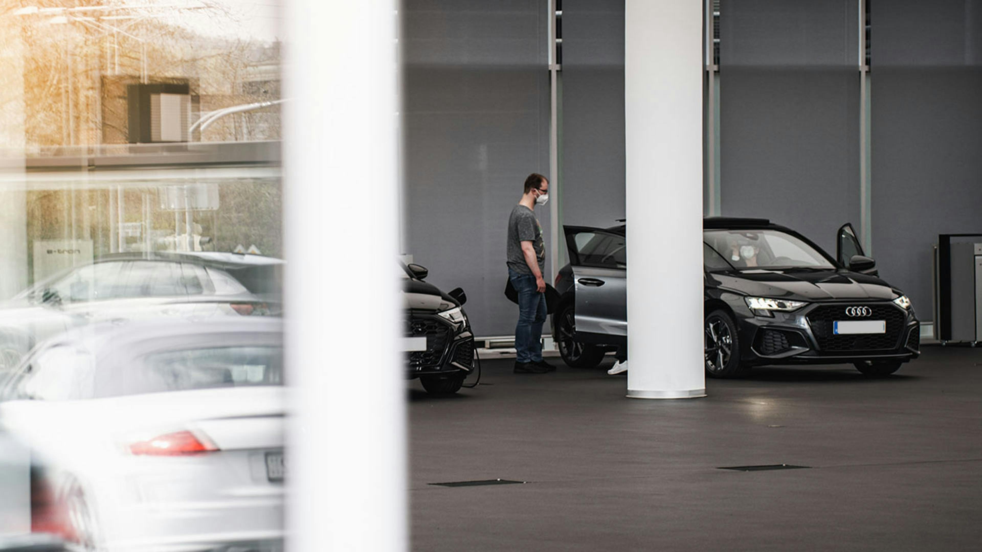 Ein Mann betrachtet einen schwarzen Audi, der in einem Autohaus steht.