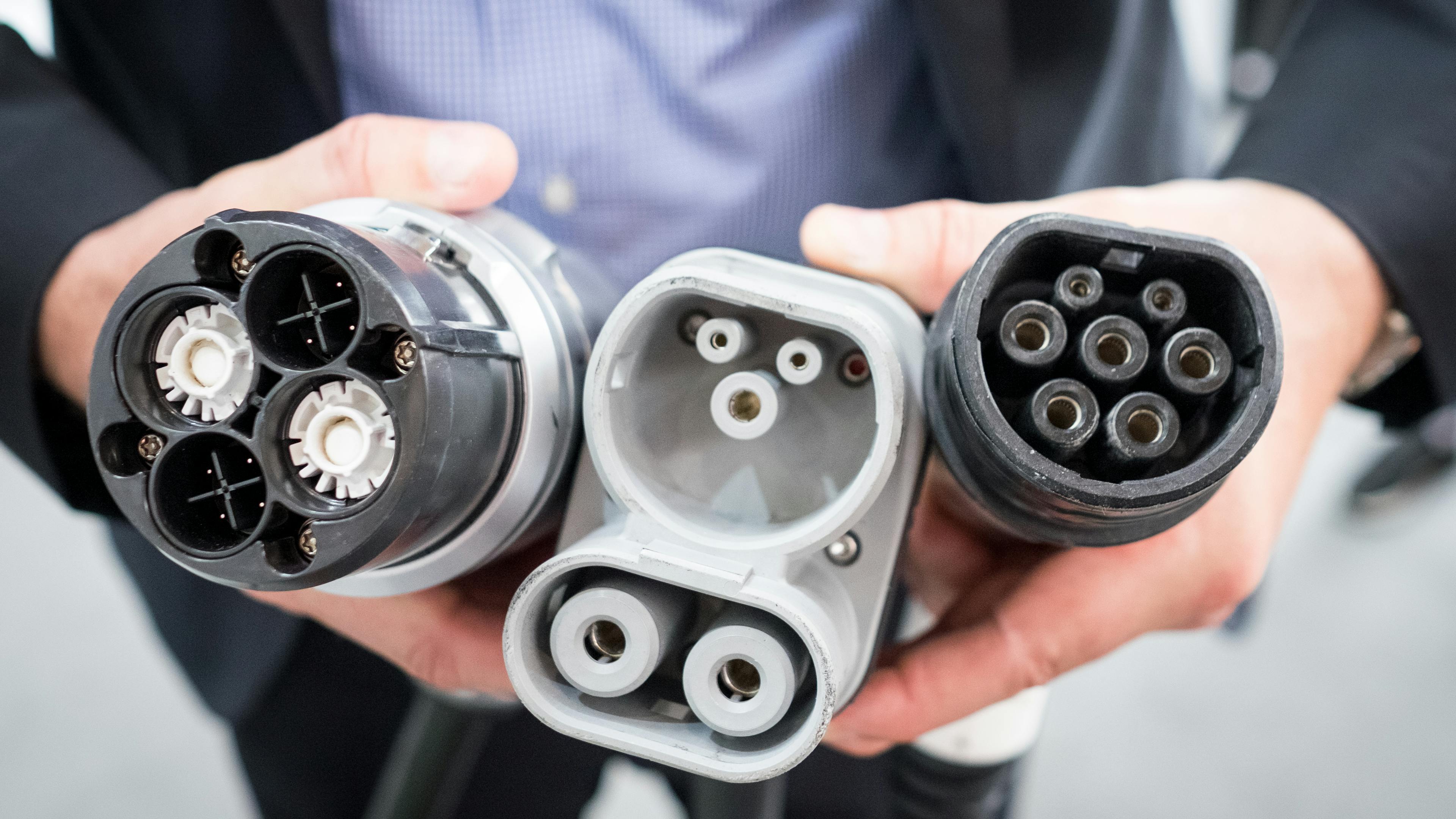 A CHadeMO plug, a combo plug and a type 2 plug are held by hands