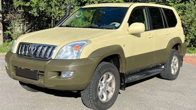 Ein gelb-grüner Toyota Land Cruiser Geländewagen steht vor Bäumen.