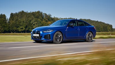 Ein blaues BMW i4 Elektroauto mit Allradantrieb fährt eine Landstraße entlang.