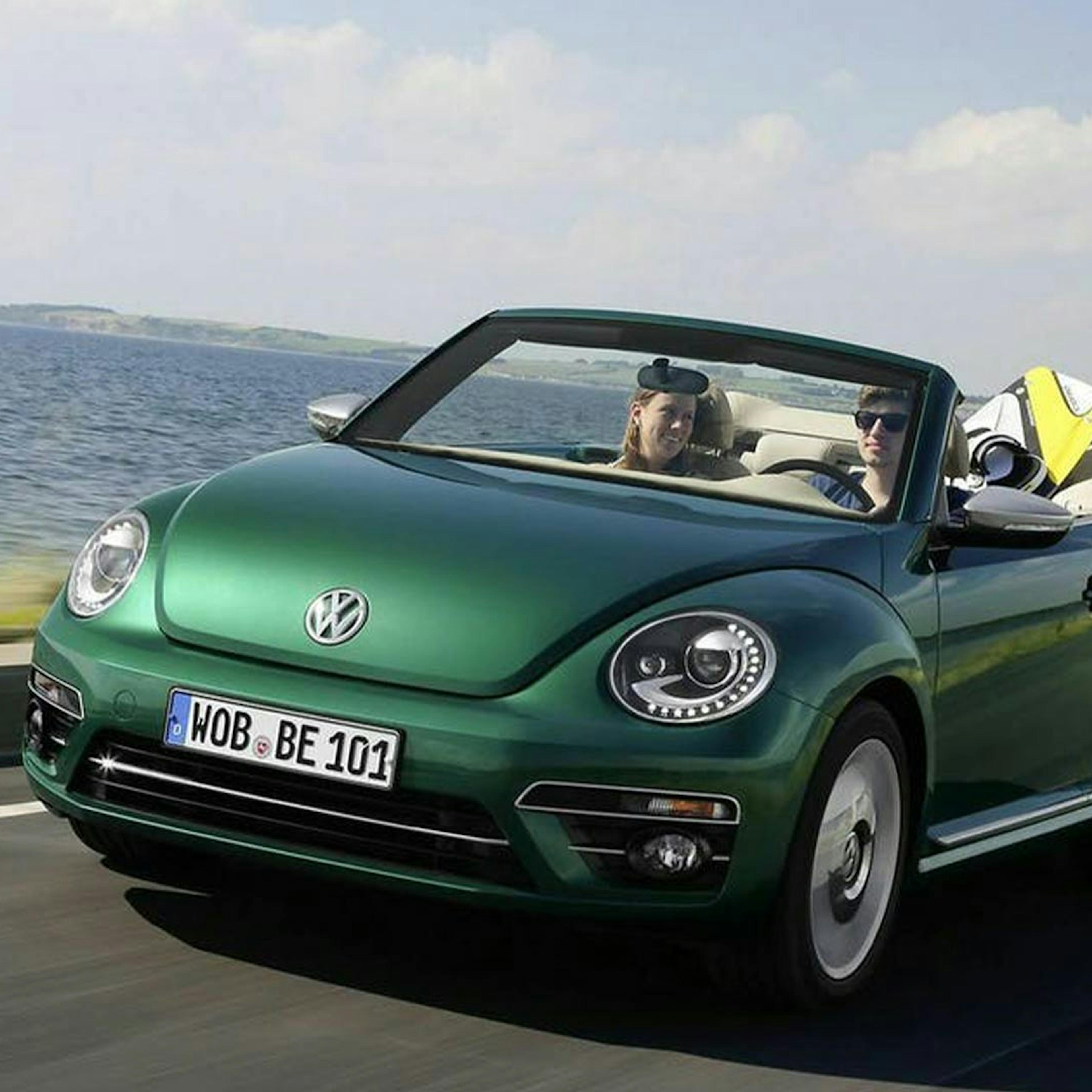 Ein grüner VW New Beetle mit geöffnetem Cabrioverdeck fährt eine Küstenstraße entlang.