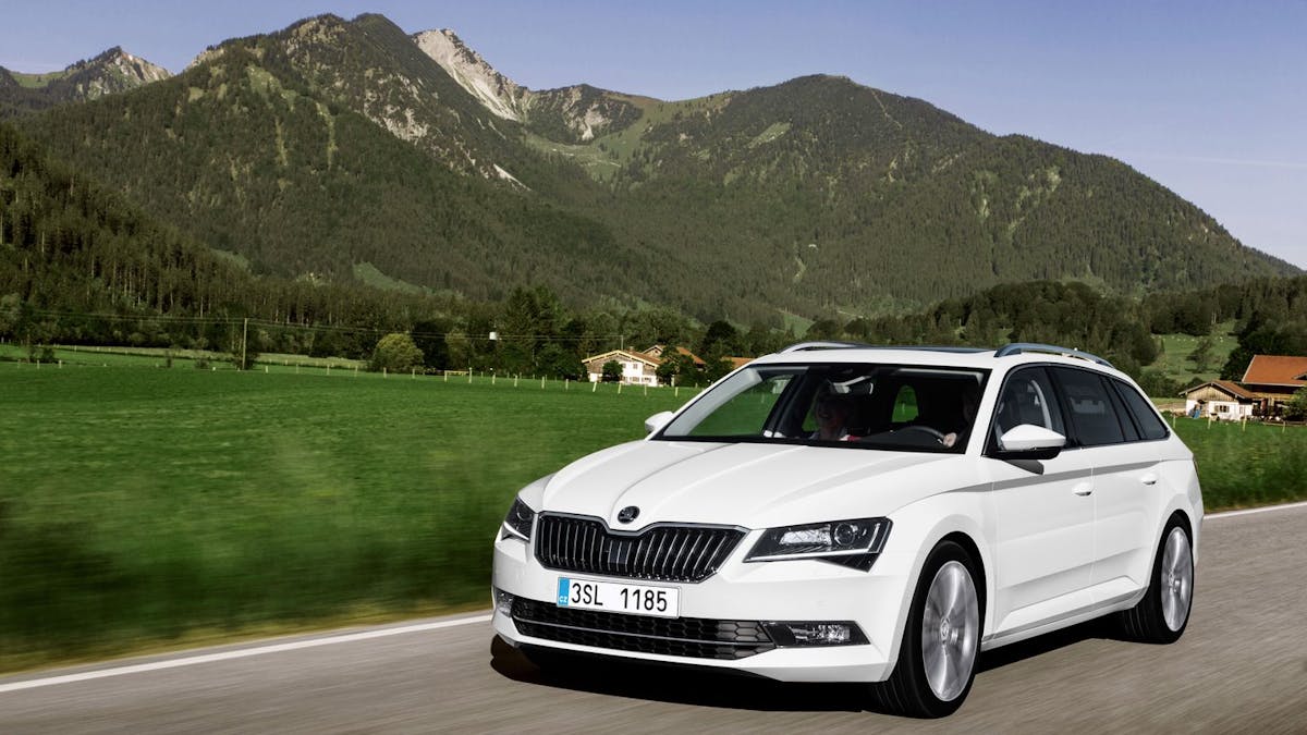 Ein weißer Škoda Superb Combi fährt an einem Bergpanorama vorbei.
