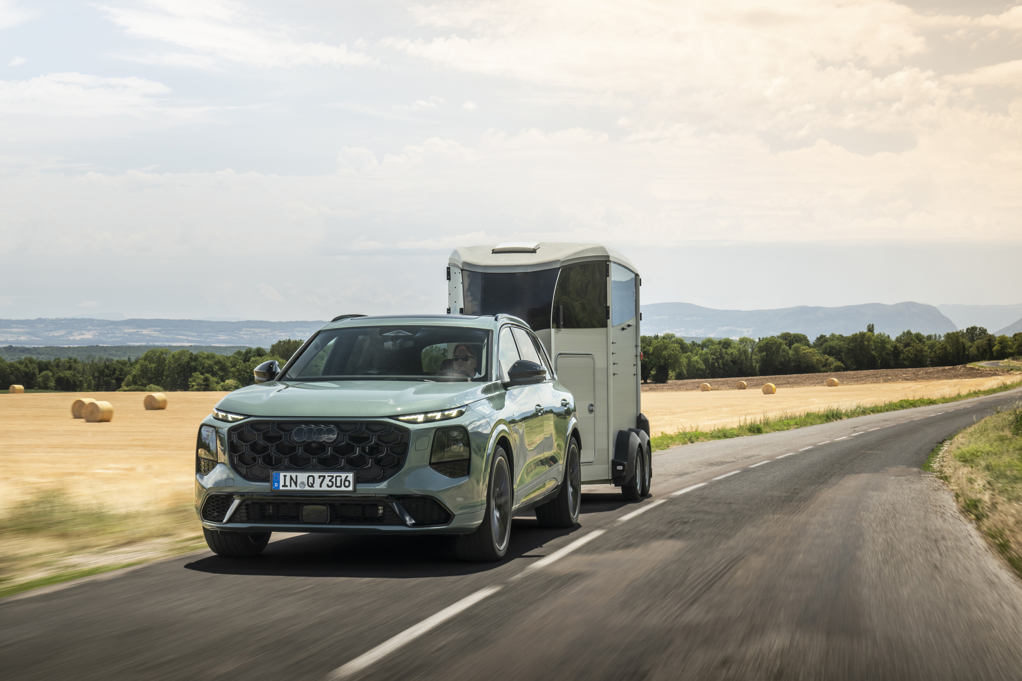 Ein Audi Q7 SUV in Agavengrün Metallic in einer Fahraufnahme mit Anhänger.