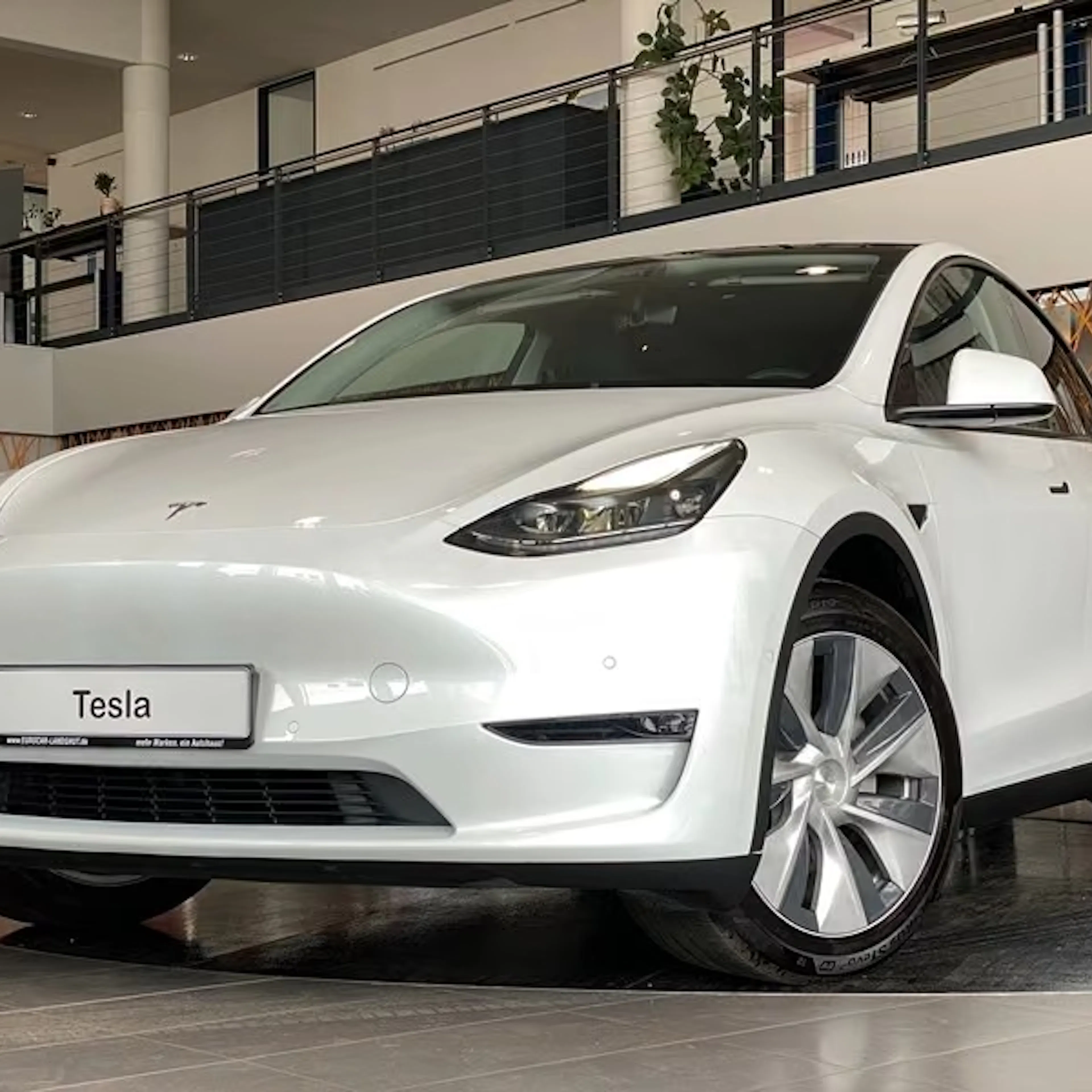 Ein weißes Tesla Model Y AWD Long Range steht in einer Verkaufshalle.