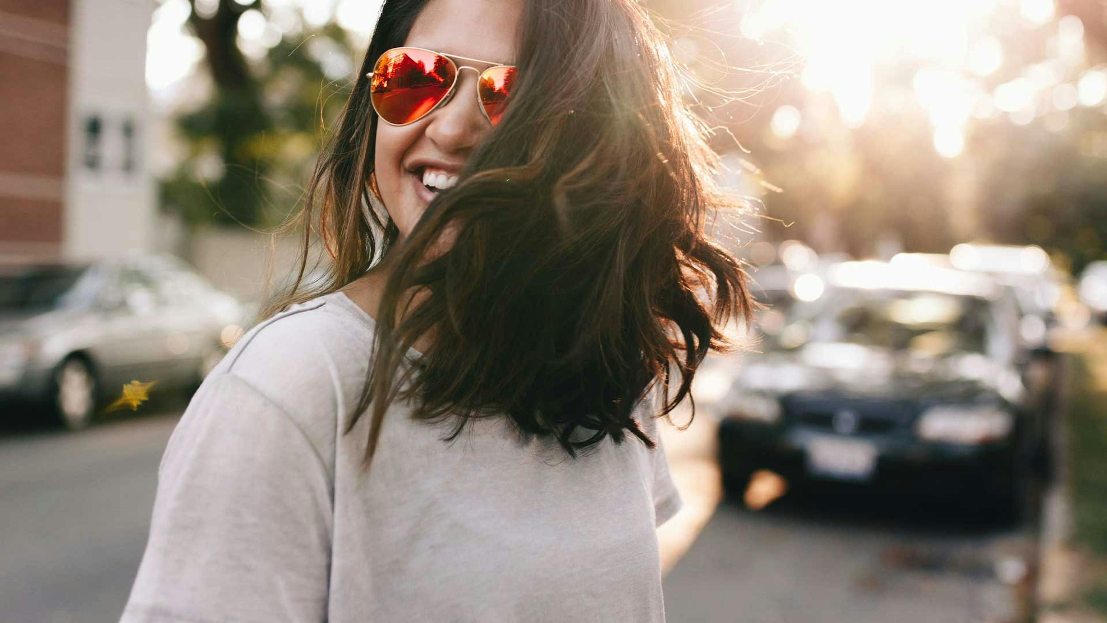 Eine junge Frau mit braunen Haaren und Sonnenbrille steht vor einem schwarzen Pkw