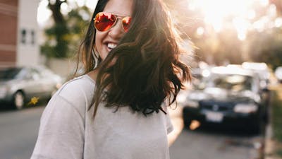 Eine junge Frau mit braunen Haaren und Sonnenbrille steht vor einem schwarzen Pkw