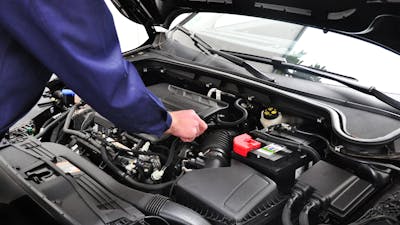 Blick in den geöffneten Motorraum eines Pkw, an dem ein Techniker arbeitet