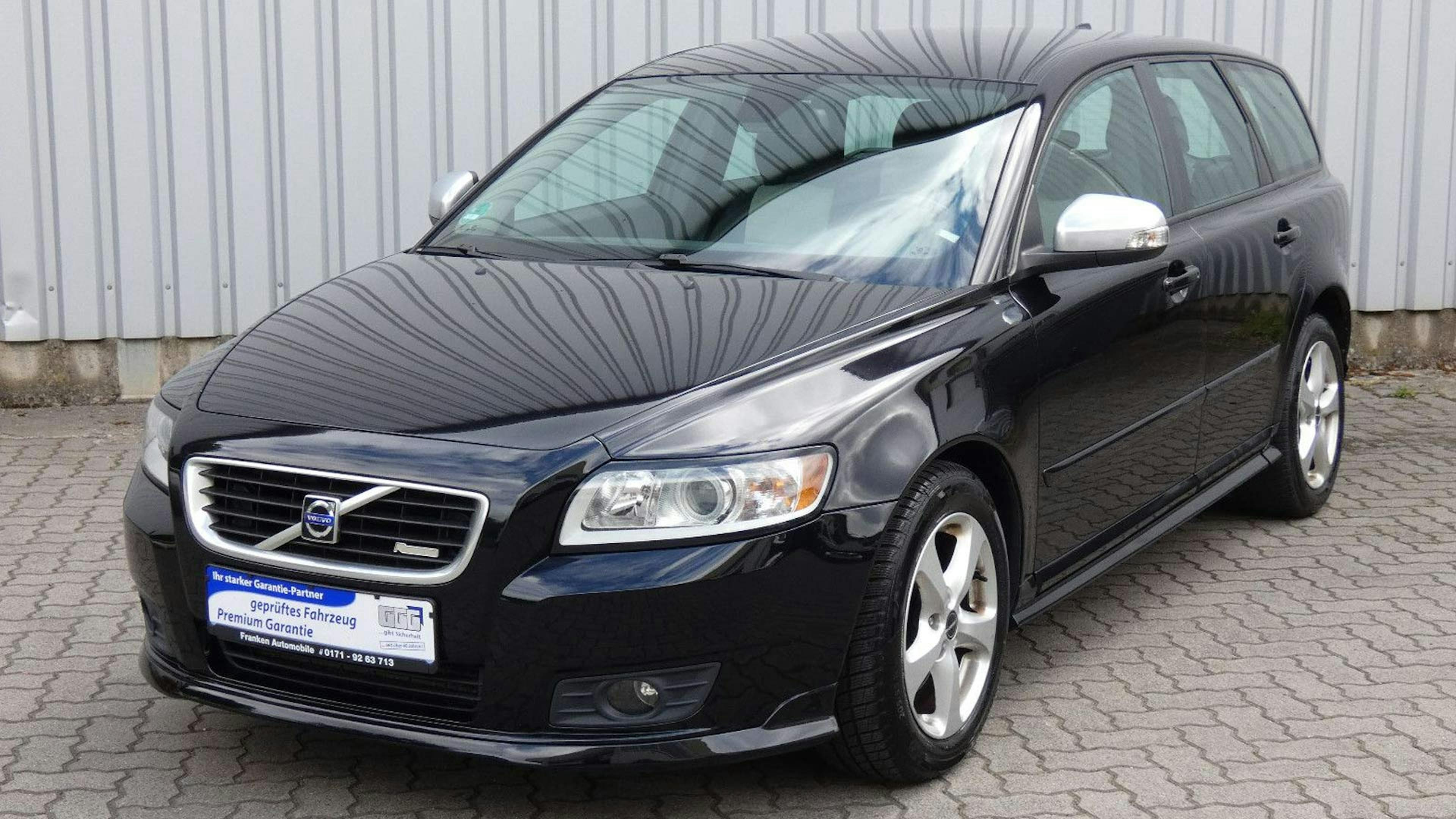 Ein schwarzer Volvo V50 Kombi steht vor einer grauen Wand.