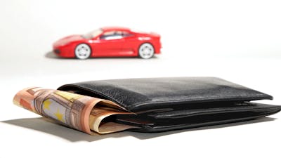 Ein brauner Geldbeutel, aus dem 50-Euro-Scheine herausragen, und ein rotes Spielzeugauto auf weißem Hintergrund
